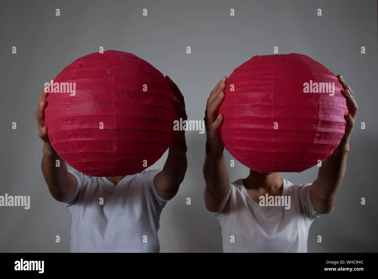 People Covering Faces With Red Paper Lanterns Against Wall Stock Photo