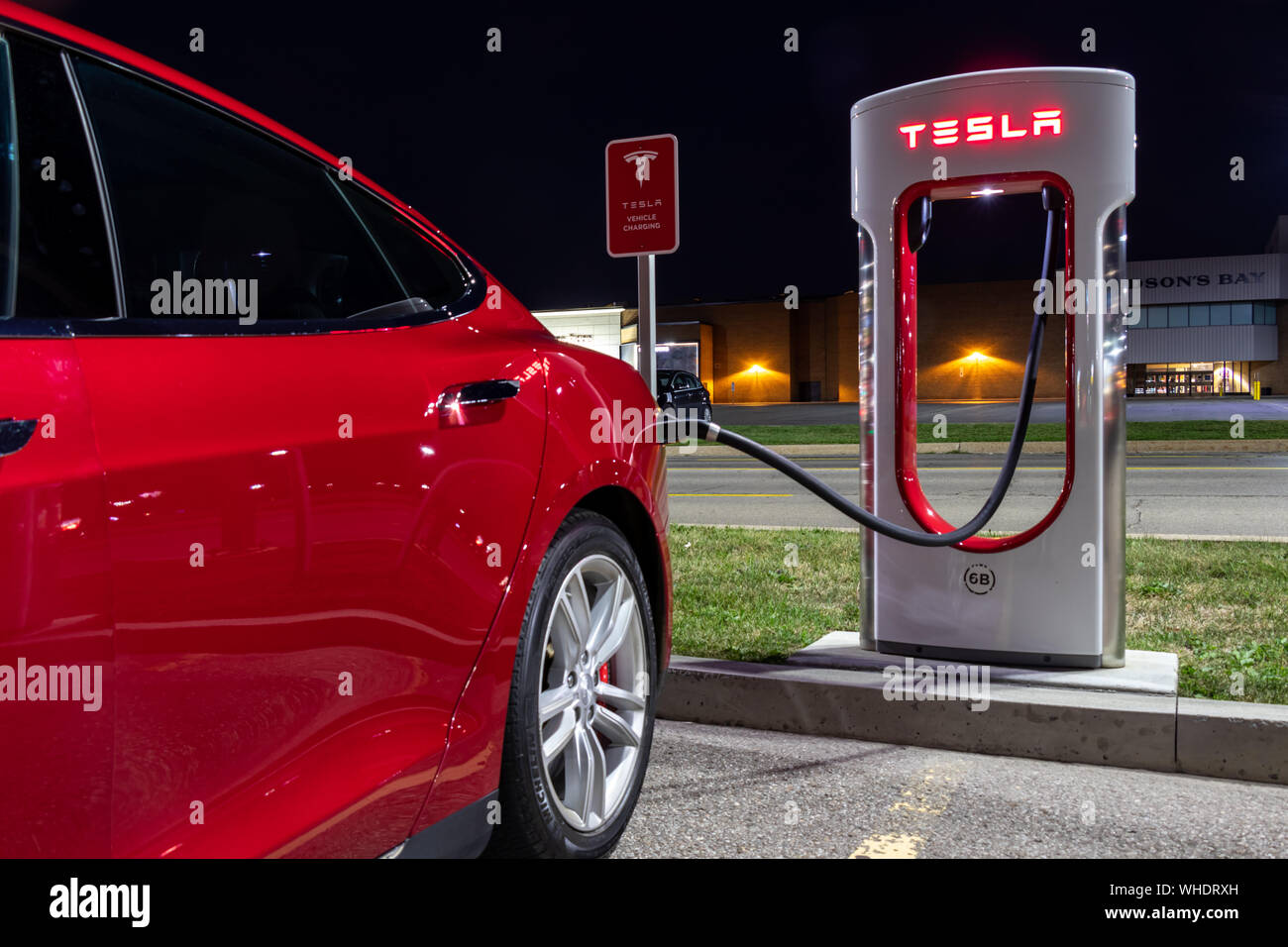 Red Tesla Model S plugged-in and charging at Tesla Supercharger late at night. Stock Photo