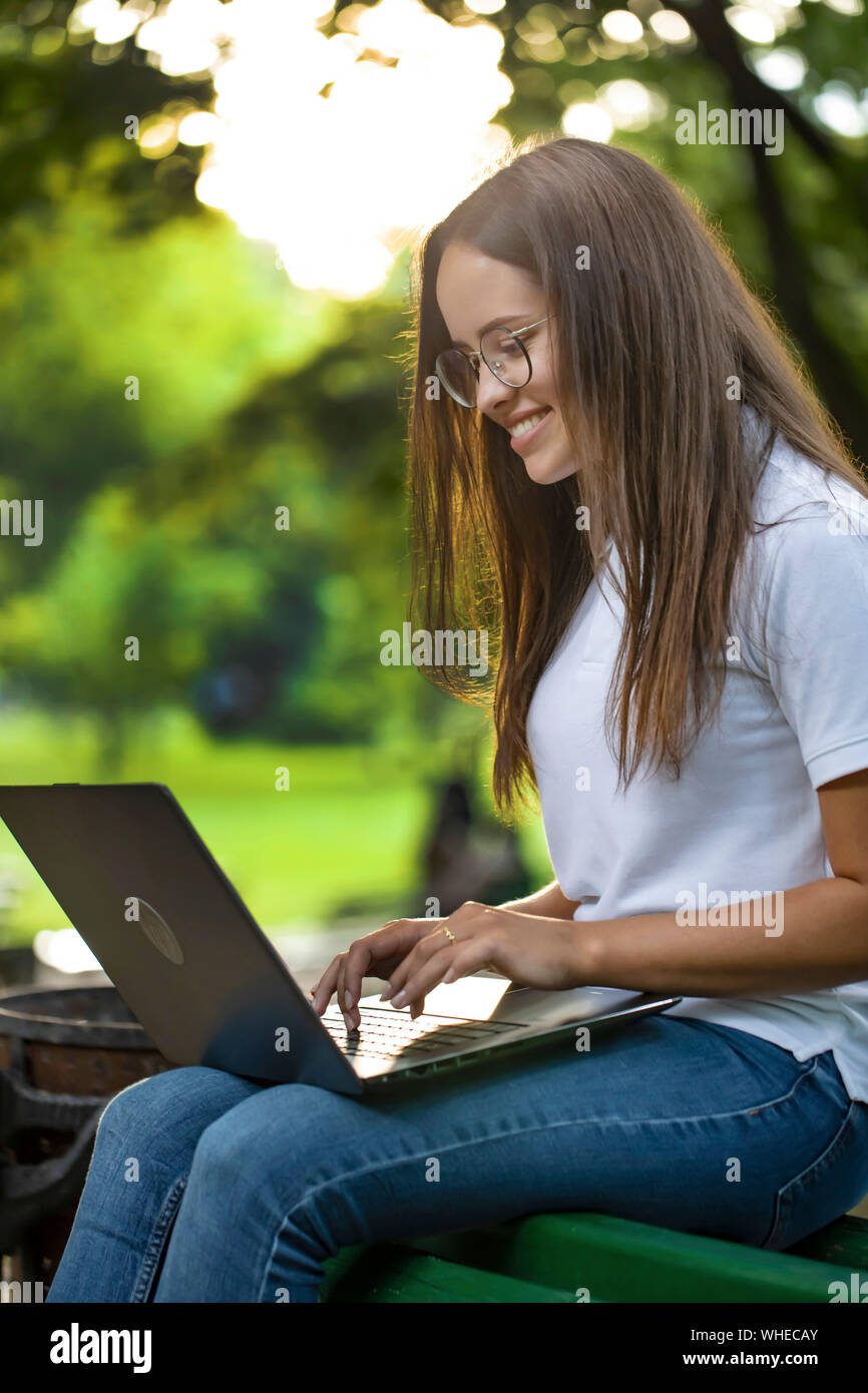 Cute student girl using laptop sitting on a bench in university park Stock Photo