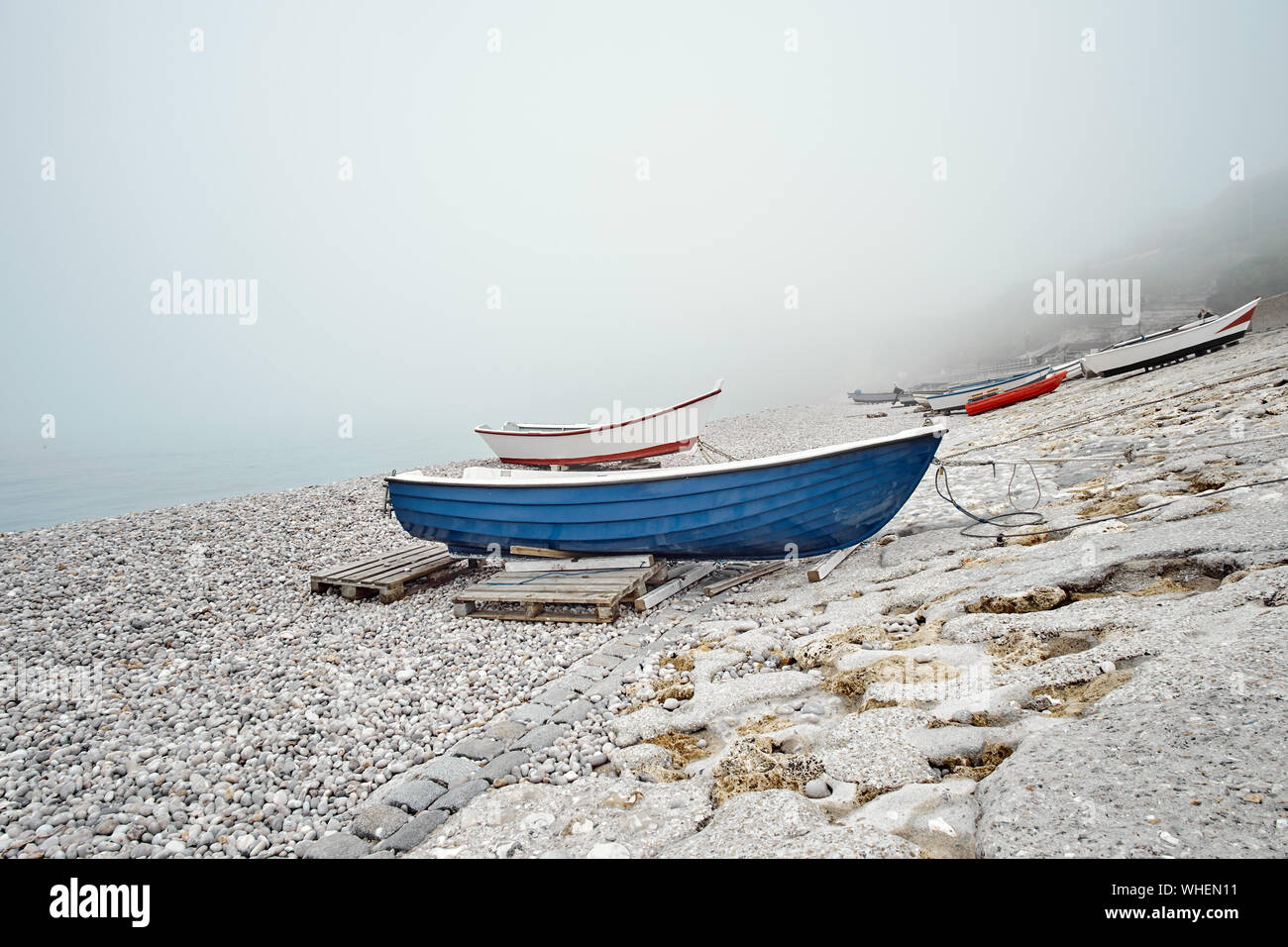 Blue and red fishing boats on a rocky pebble beach in the early morning ...