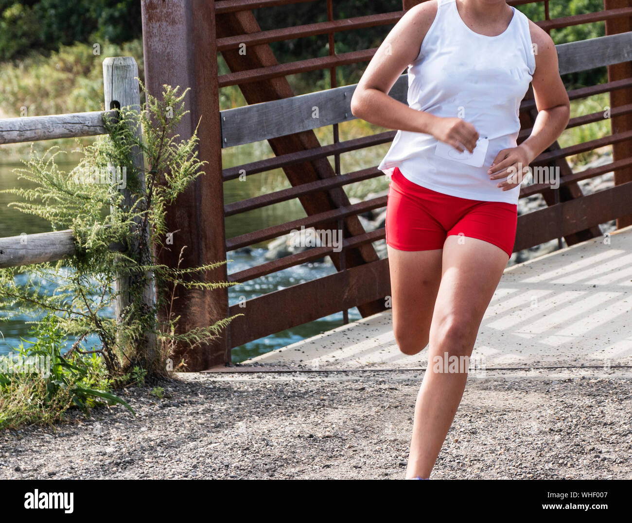 A high school girl crossing over a bridge with water in the background at Sunken MEadow State Park during a cross country race in the fall. Stock Photo