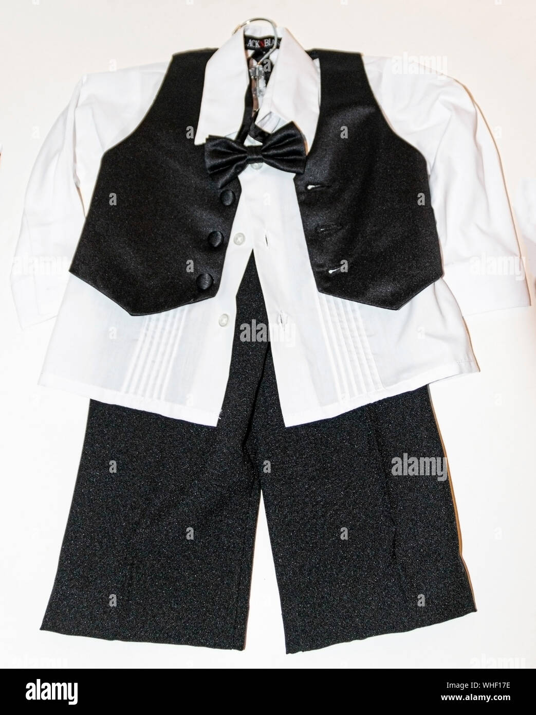 Toddlers tuxedo with a black vest over a white shirt with a white backgound hanging on a hanger with no jacket. Stock Photo