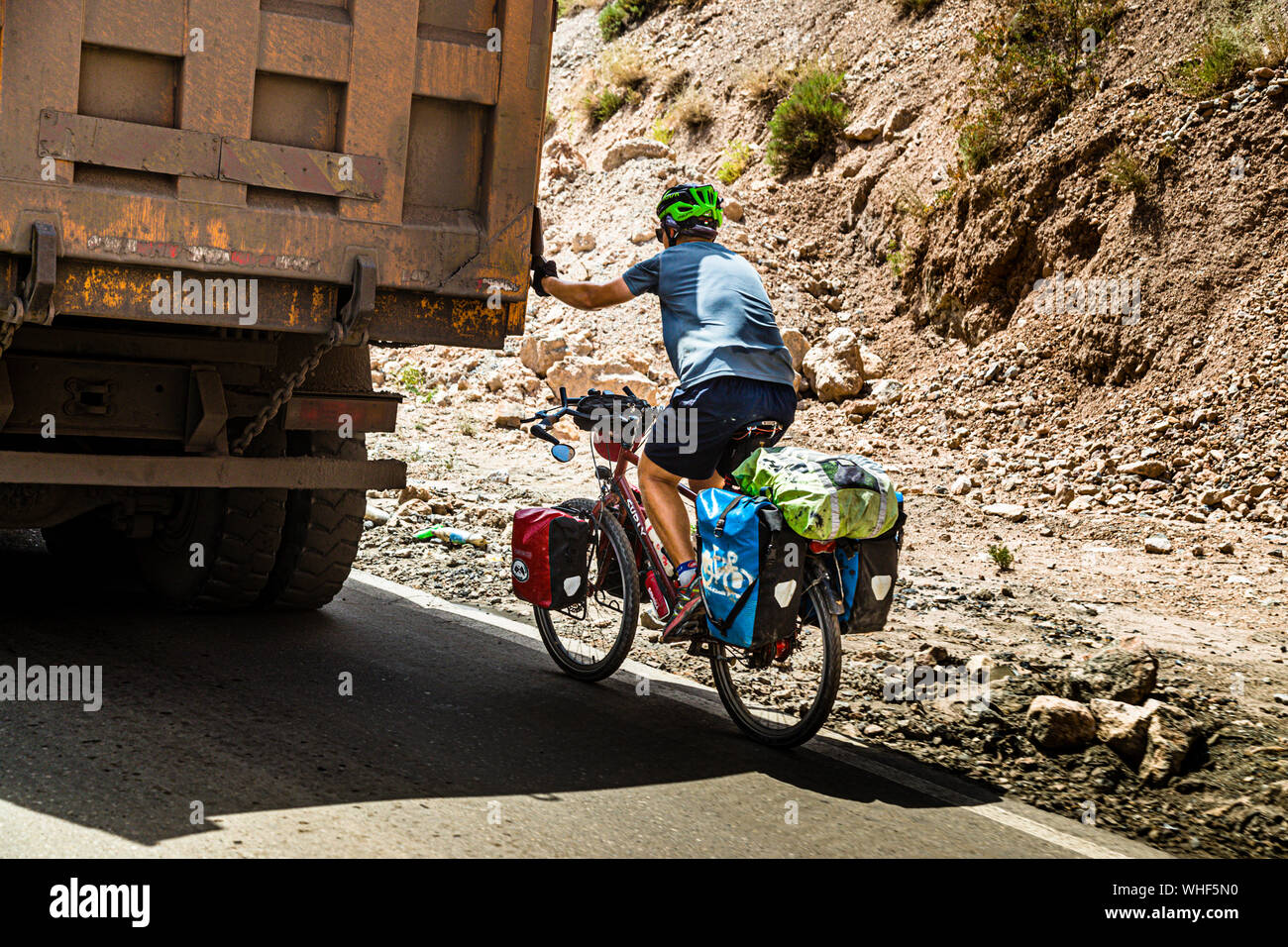 Cyclist being pulled by Van up a Mountain Pass near Takfon, Tajikistan. A bicycle tourist is pulled up the Takfon Pass by a truck in Tajikistan. In the tow of a transporter, several hundred meters of altitude can easily be overcome on a bicycle Stock Photo