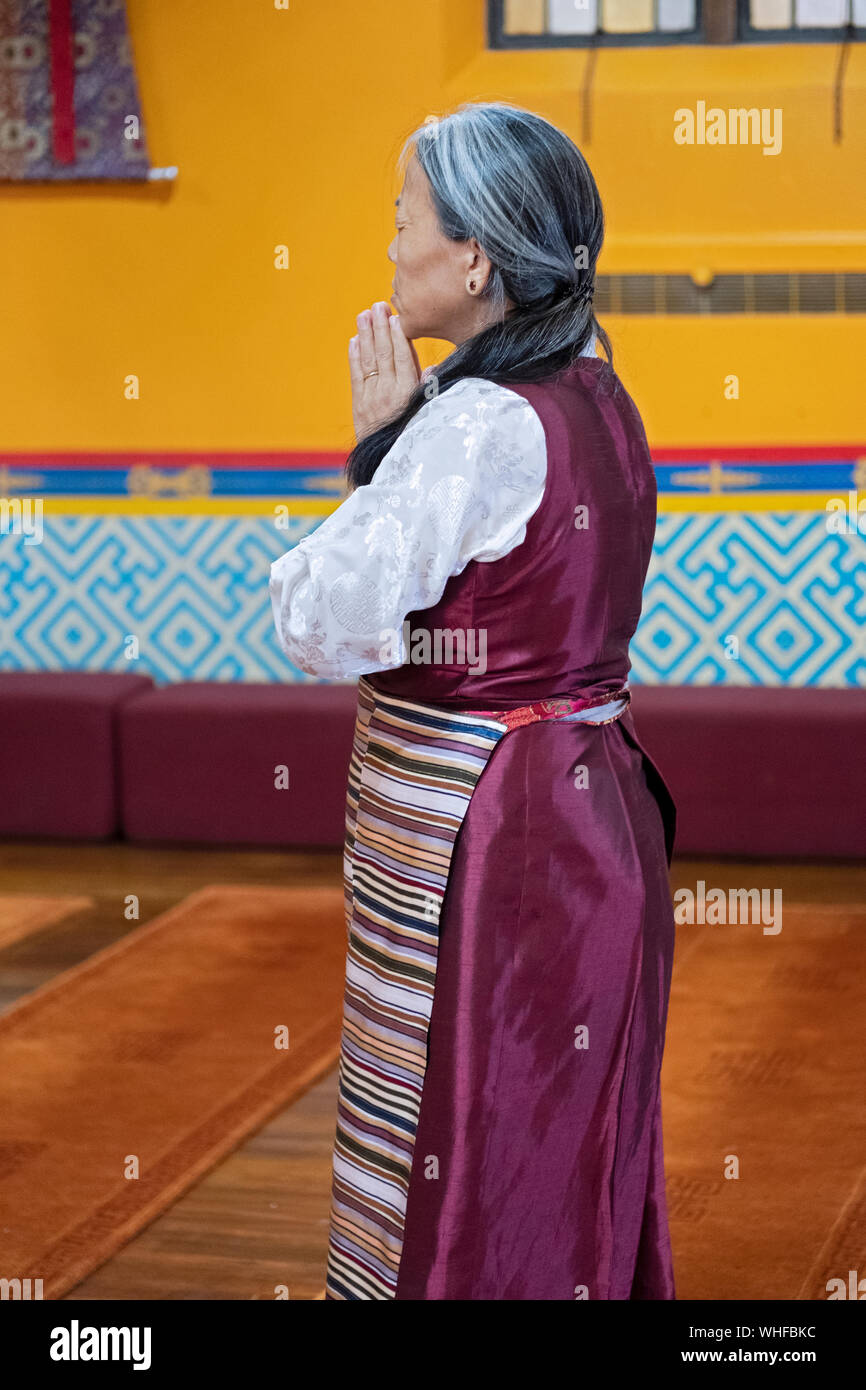 A devout Buddhist woman stops for prayer & meditation upon entering a temple. In Elmhurst, Queens, New York City. Stock Photo