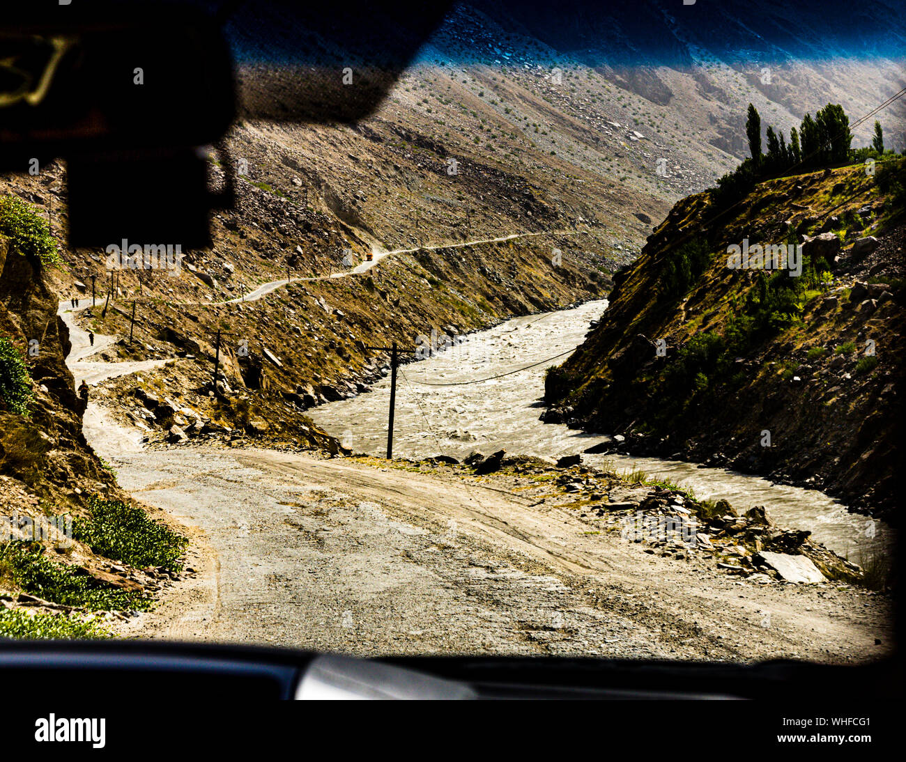 A gravel road winds down to the Panj River on the border between Tajikistan and Afghanistan, a footpath running along the slope. Stock Photo