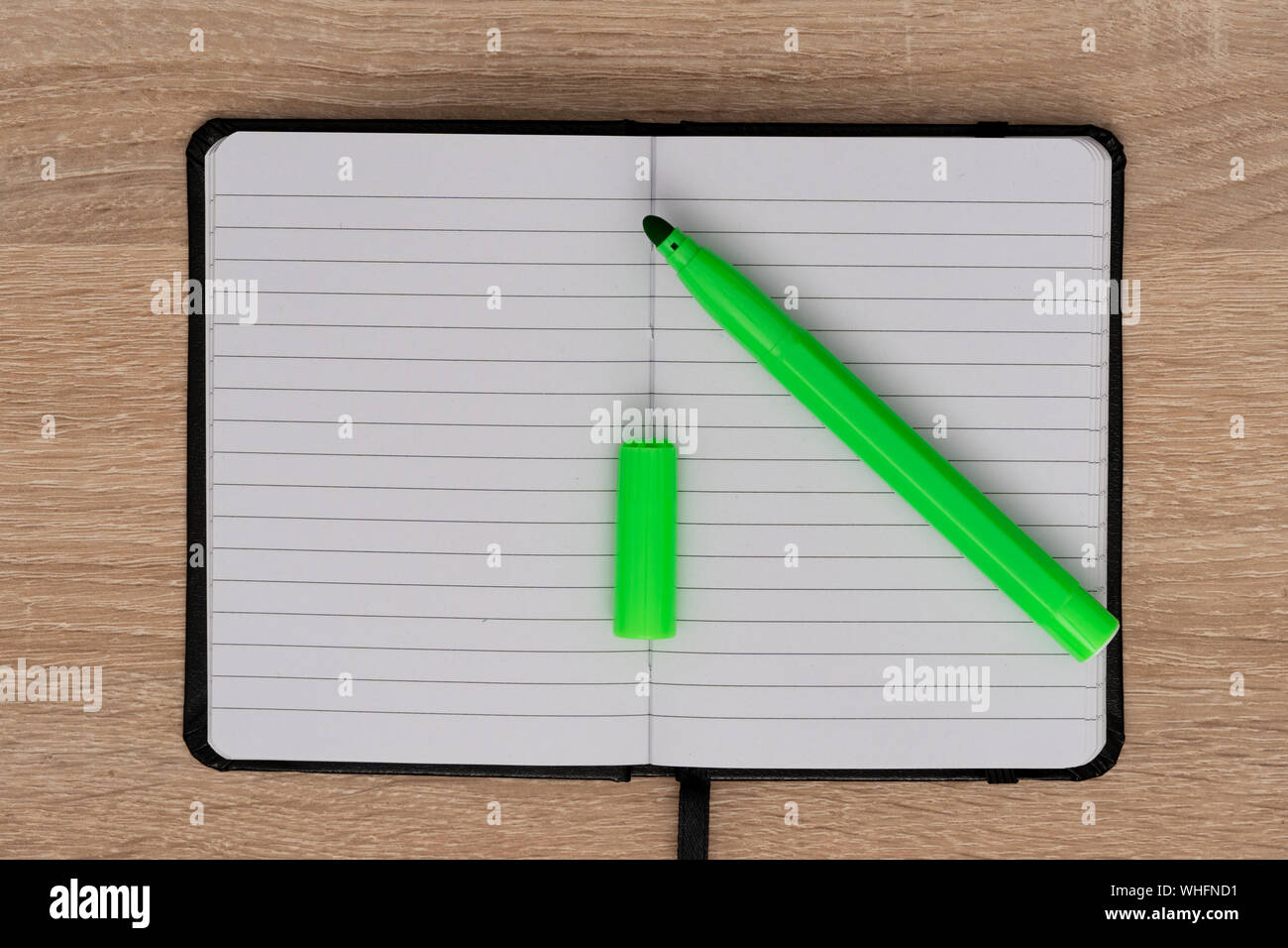 Green marker and opened notebook on desk Stock Photo