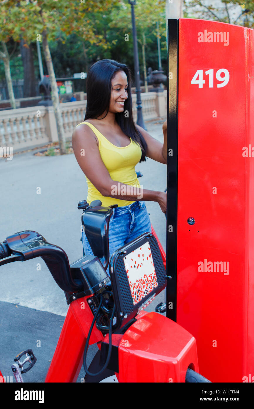 Young latin girl renting a bike from a bike stand on the street Stock Photo
