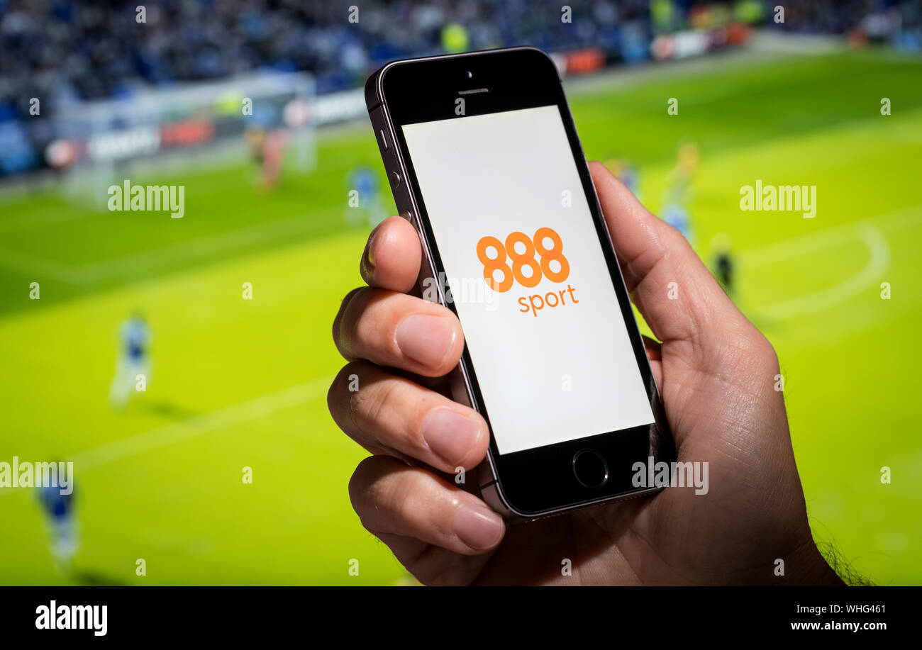 A man looking at the 888 Sport app website whilst watching the football Stock Photo