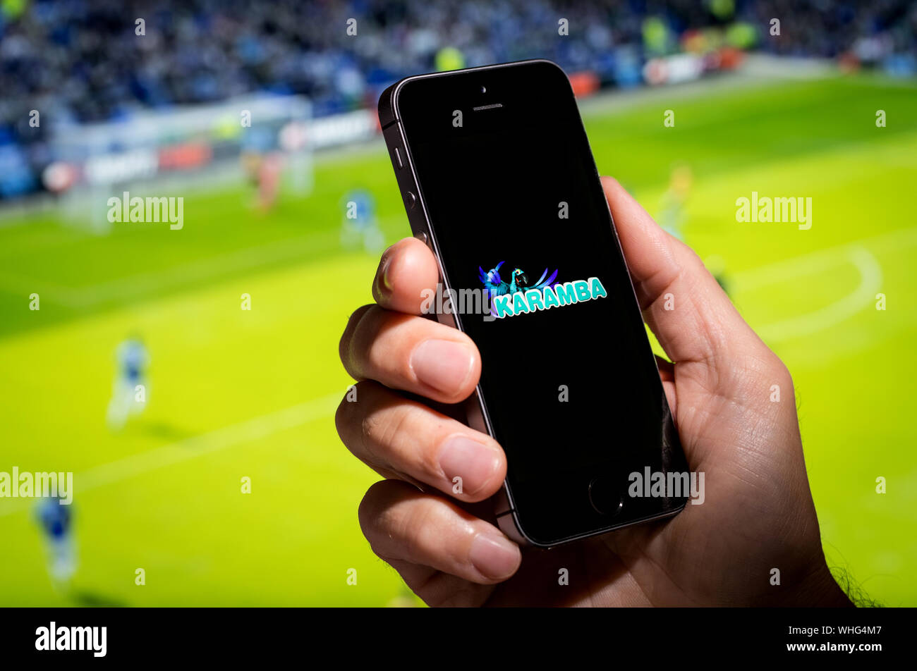 A man looking at the Karamba betting app website whilst watching the football Stock Photo