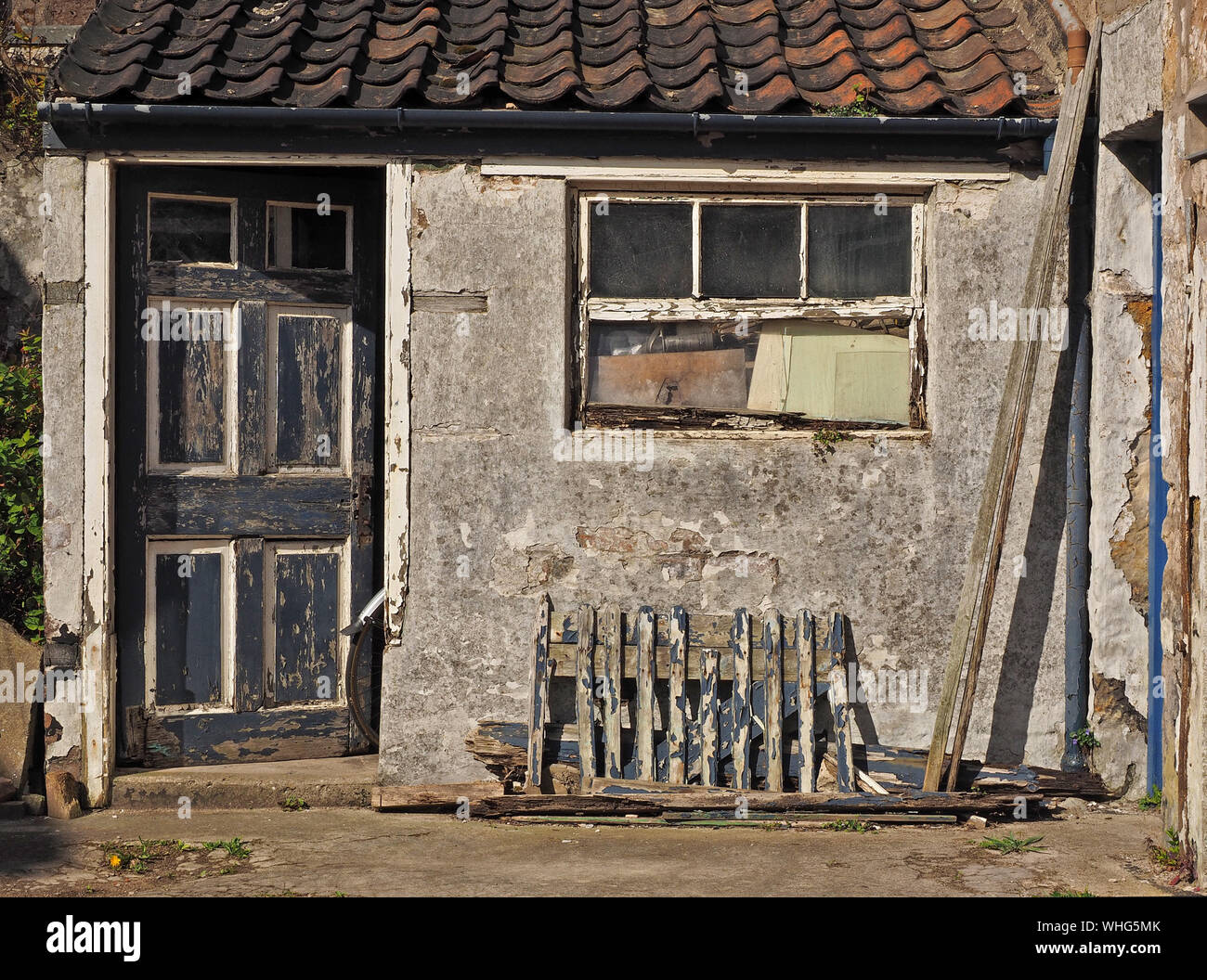 a bicycle rear wheel & mudguard protrude from the door of a distressed outhouse with dilapidated woodwork at Anstruther, East Neuk,Fife,Scotland,UK Stock Photo