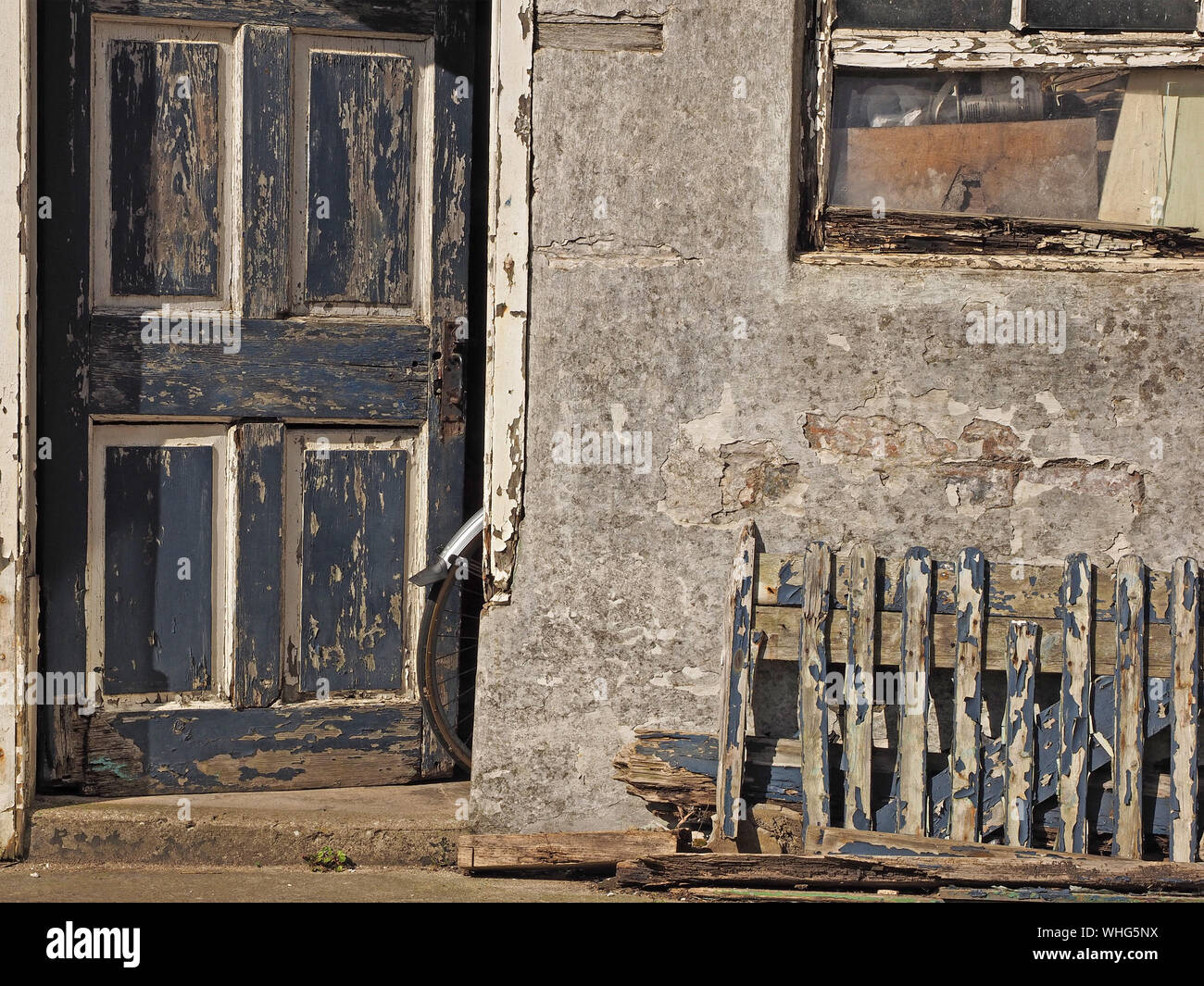 a bicycle rear wheel & mudguard protrude from the door of a distressed outhouse with dilapidated woodwork at Anstruther, East Neuk,Fife,Scotland,UK Stock Photo