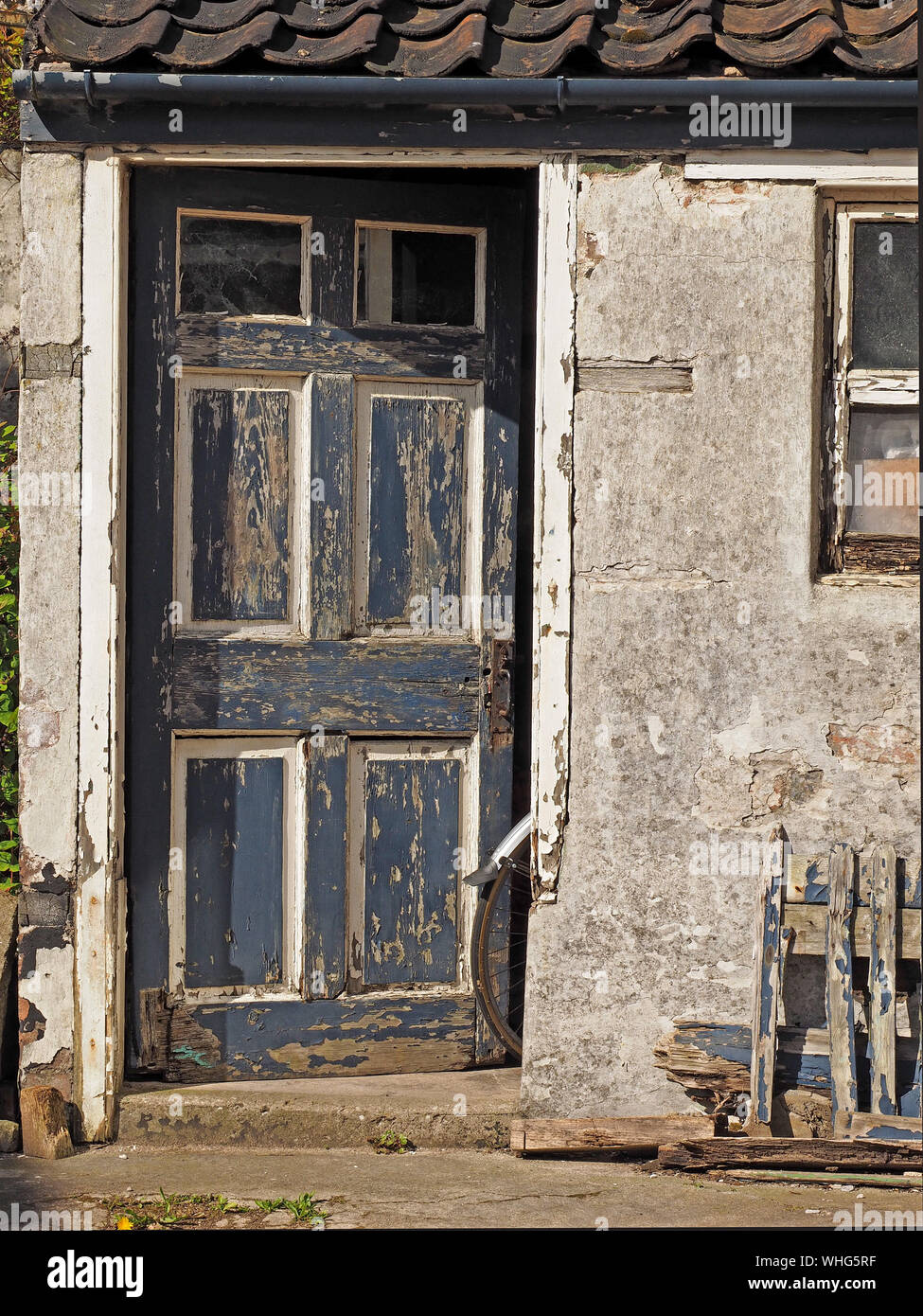 a bicycle rear wheel & mudguard protrude from the door of a distressed outhouse with dilapidated woodwork at Anstruther, East Neuk,Fife,Scotland,UK Stock Photo