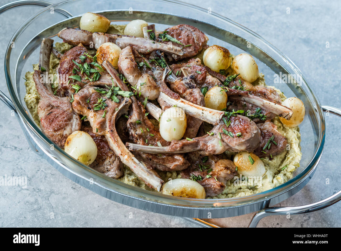 Lamb Chops with Shallots, Green Pea Hummus and Fresh Thyme Leaves served in Big Glass Tray Plate. Organic Meat Food. Stock Photo