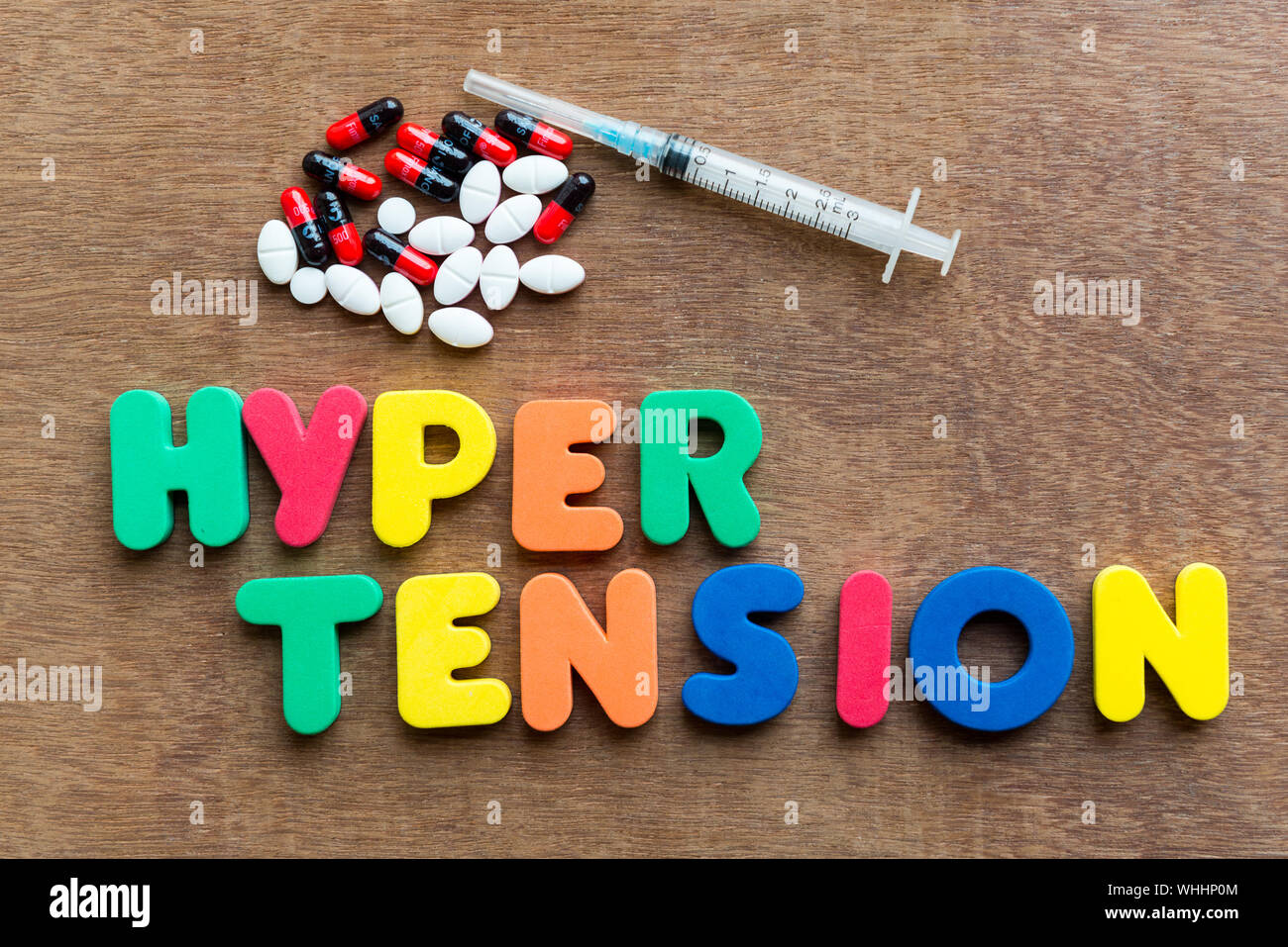 High Angle View Of Colorful Hyper Tension Text With Syringe And Pills On Wooden Table Stock Photo
