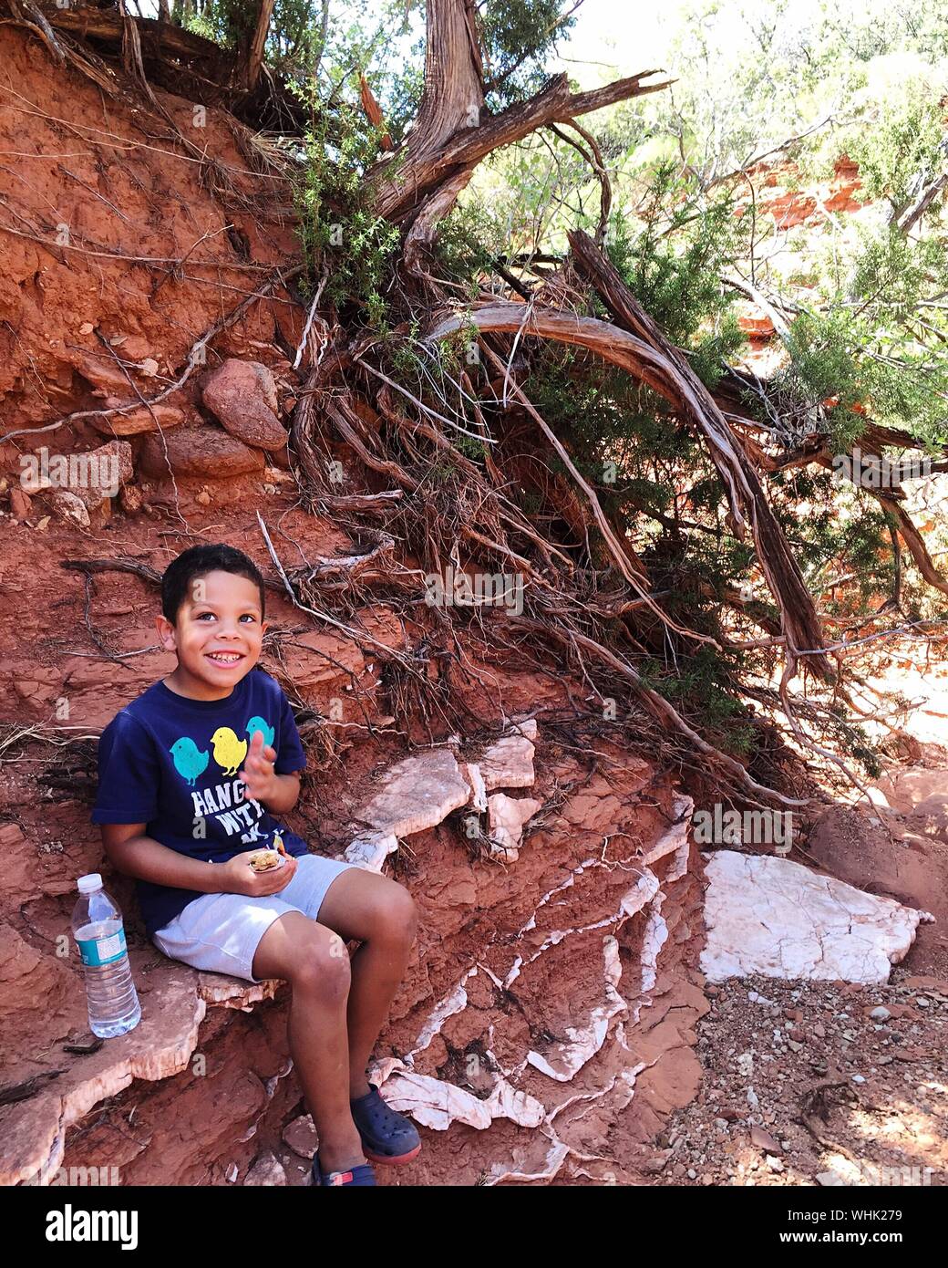 Happy Boy Sitting On Rock Formation Stock Photo
