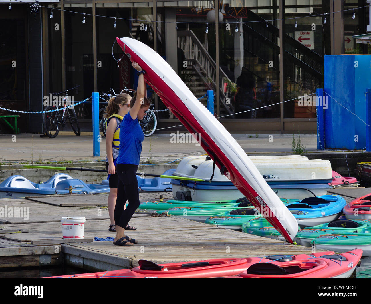 Female boat rental employee launching a red kayak from the dock at Dow