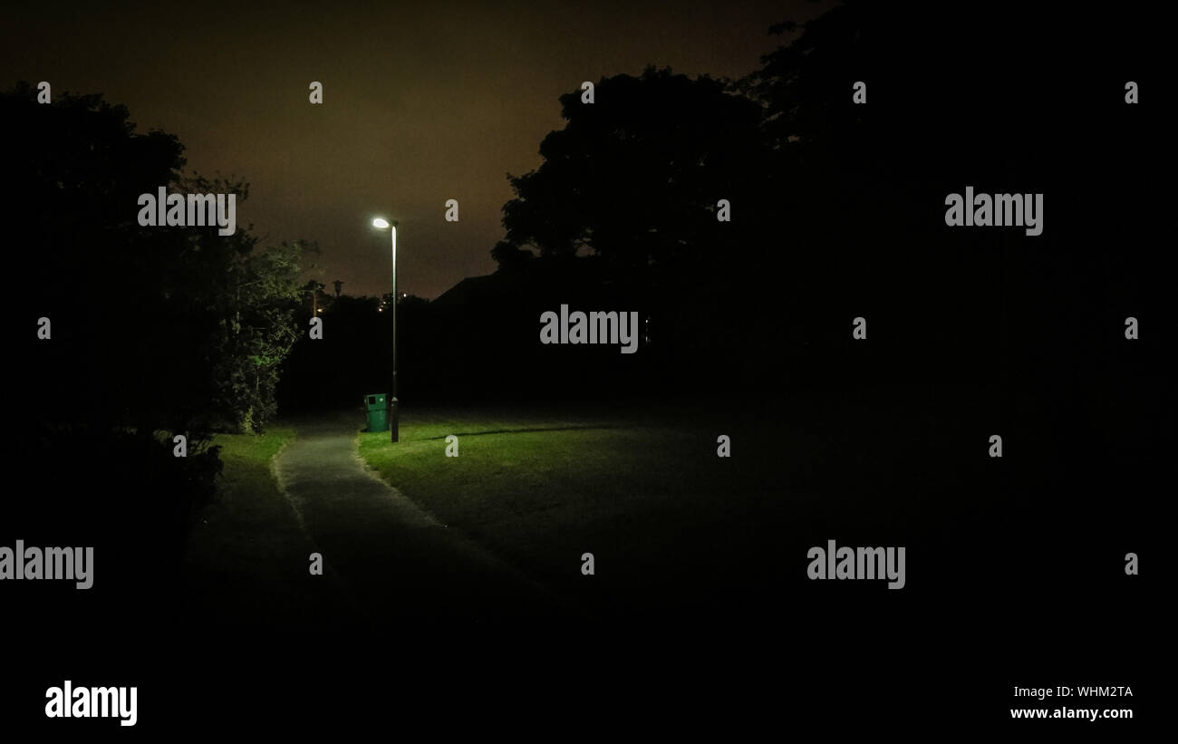Illuminated Street Light On Field By Empty Road At Night Stock Photo