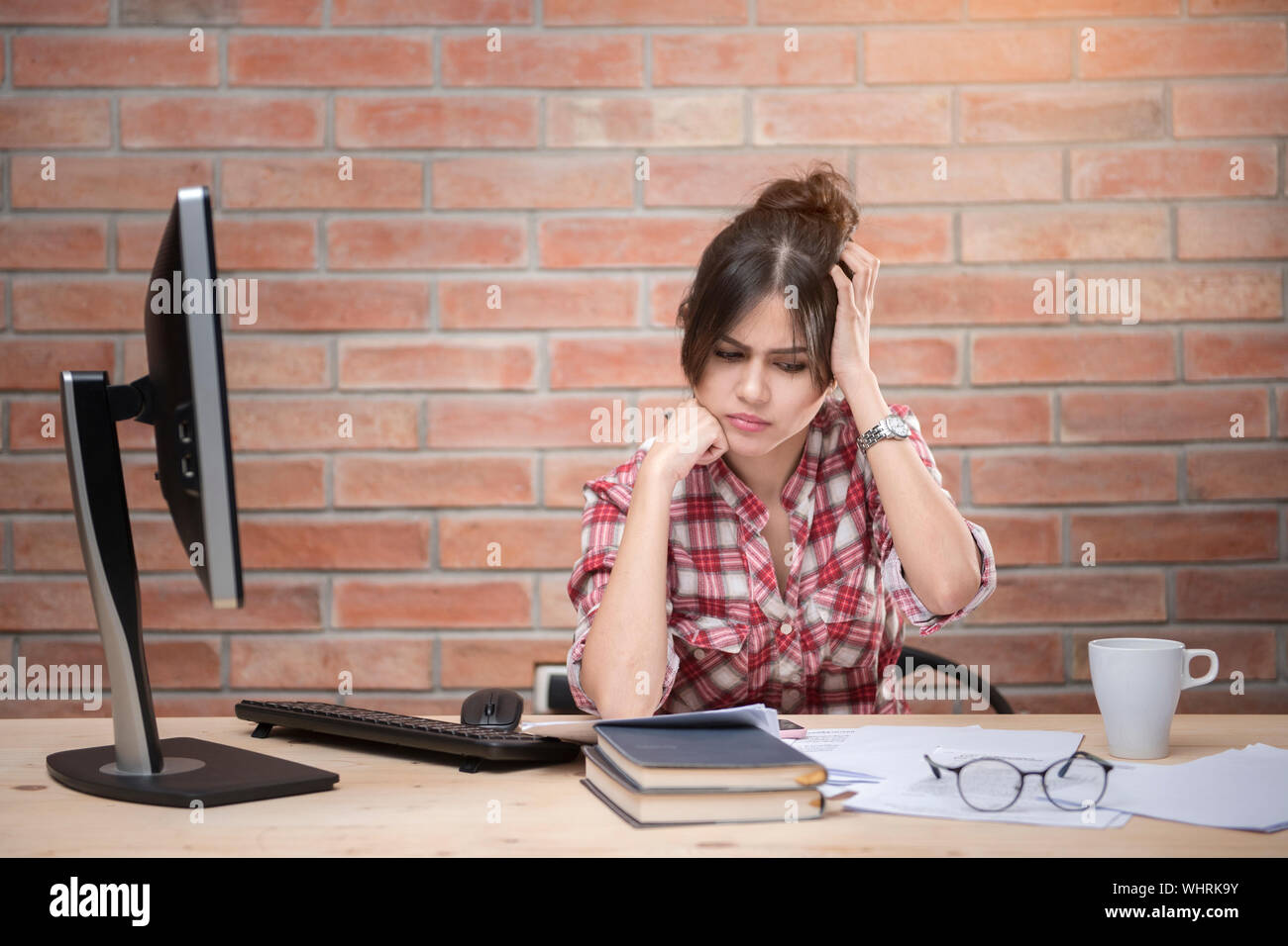 Stressed Beautiful Businesswoman With Hand In Hair Sitting At Desk Against Brick Wall Stock Photo
