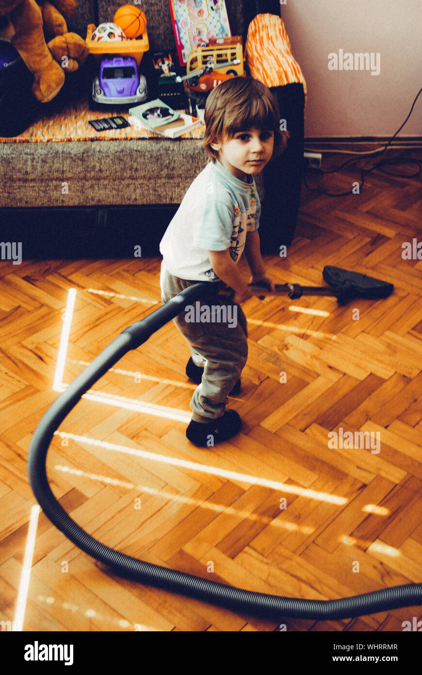Full Length Portrait Of Boy Using Vacuum Cleaner On Floor At Home Stock Photo