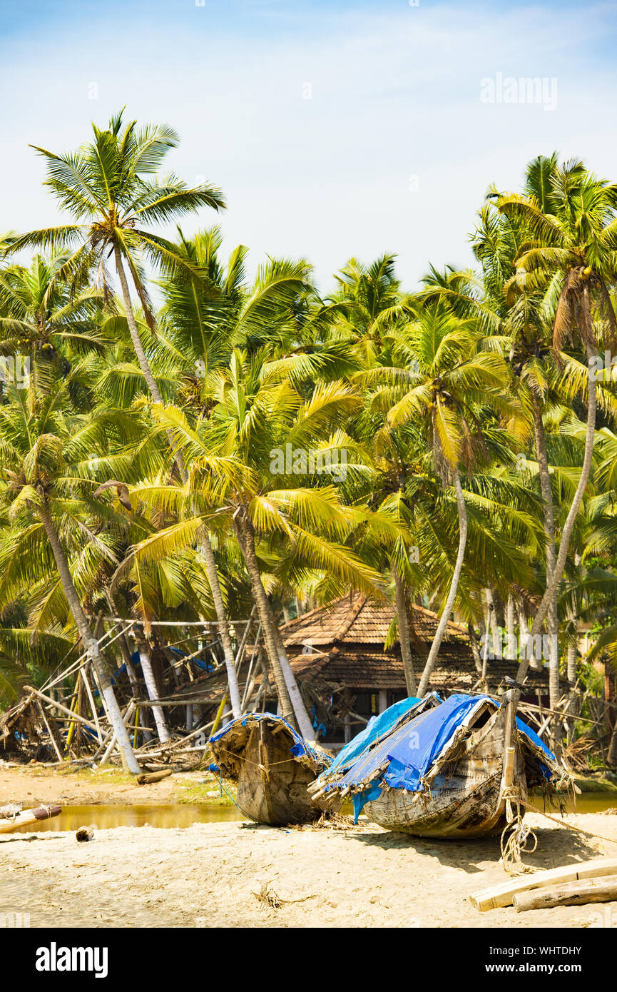 Stunning view of a beach with a wooden boat in front of a fishing village surrounded by beautiful palm trees. Varkala, Kerala, India. Stock Photo
