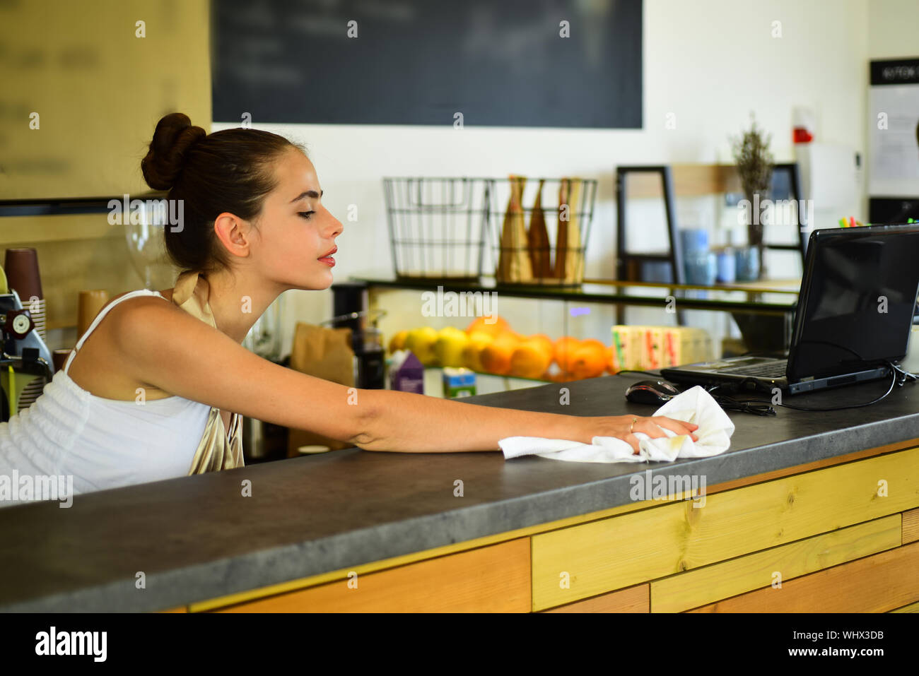 Smiling female bartender wiping glass with towel. Woman barista at