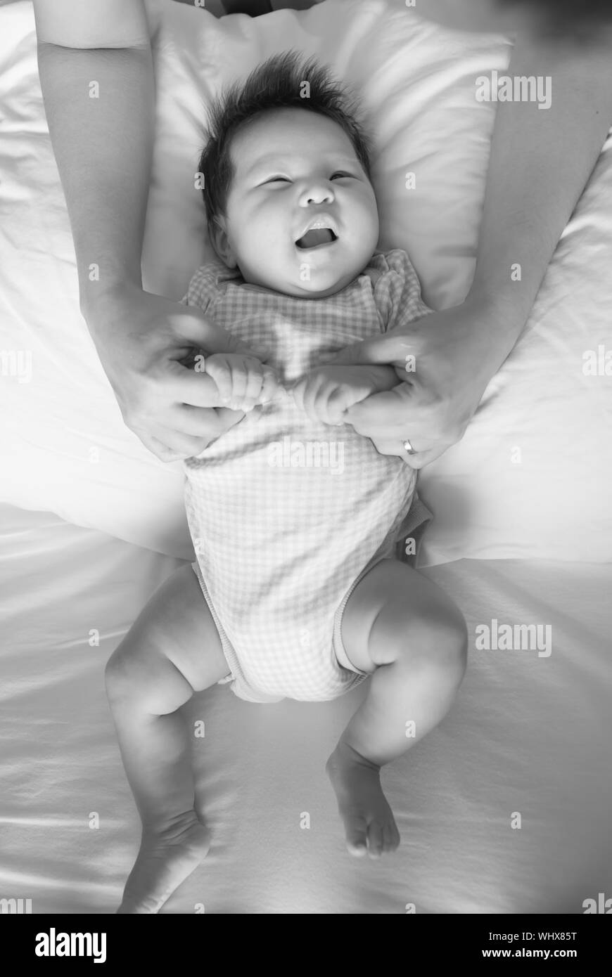 Parent spending time with their laughing baby during playtime on a bed in black and white. Stock Photo