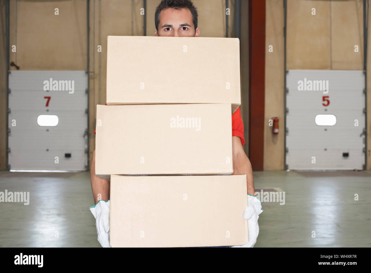 Warehouse worker carrying boxes against loading dock doors Stock Photo ...