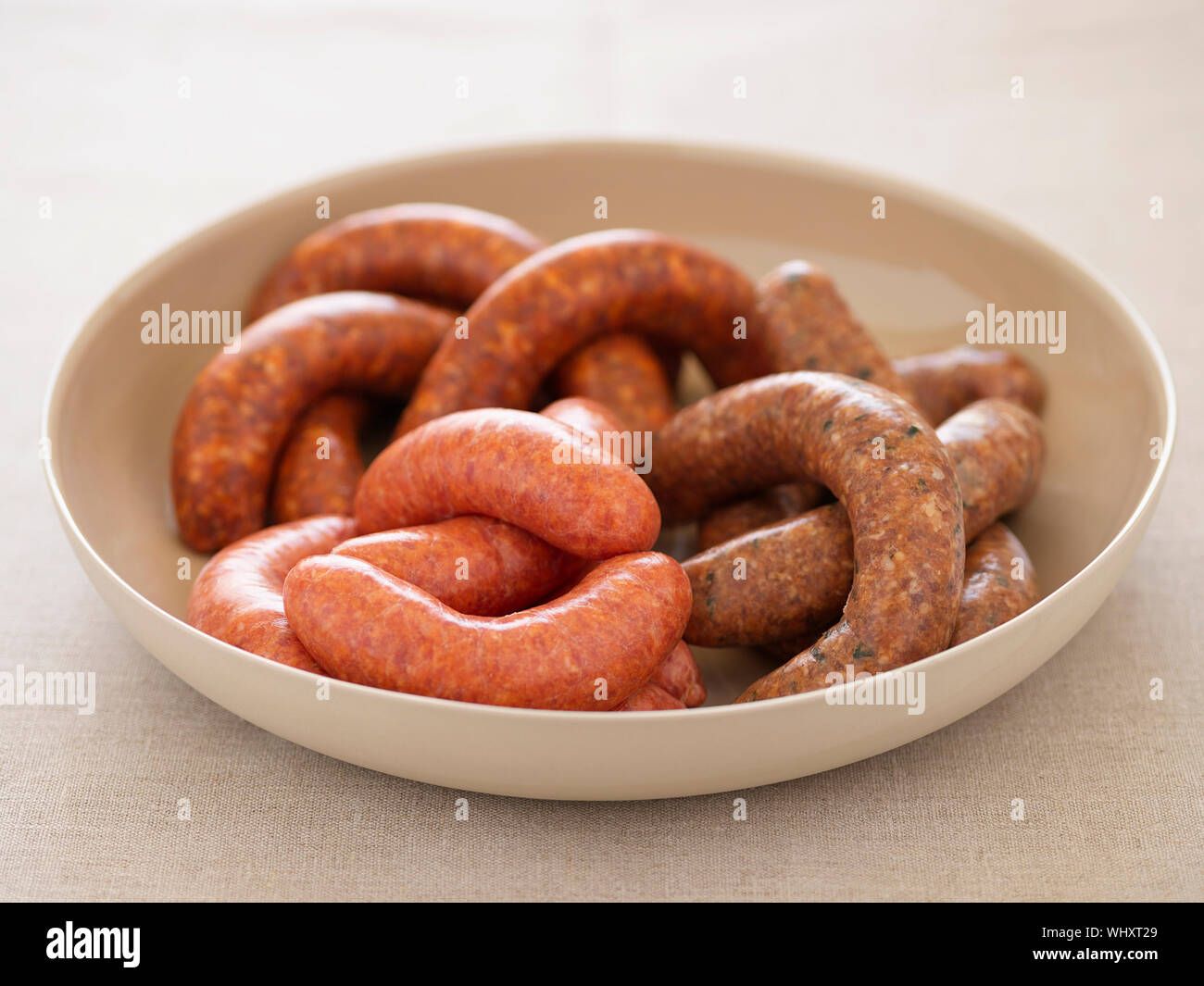 Closeup of a variety of sausages in bowl against colored background Stock Photo
