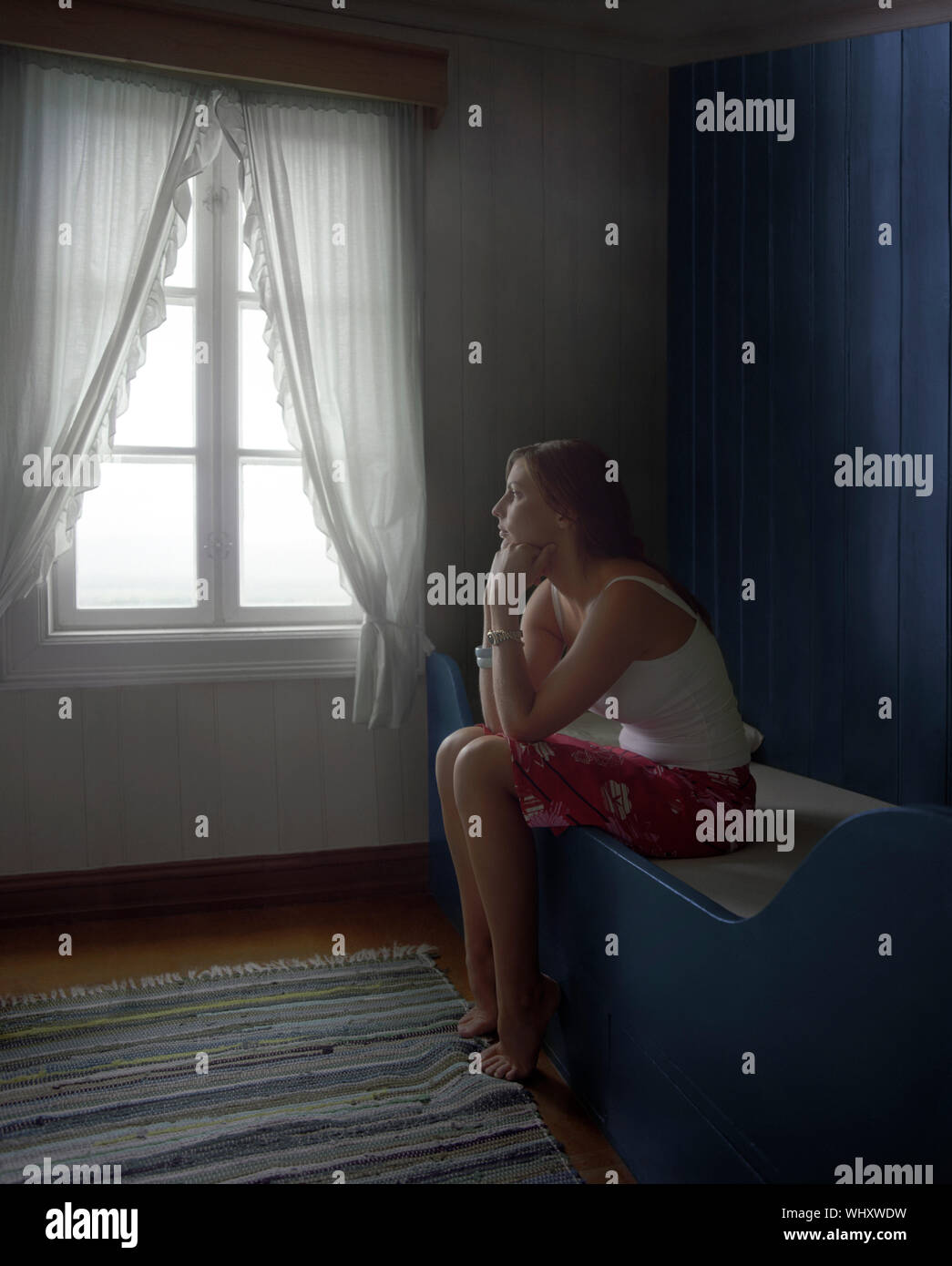Side view of a young thoughtful and sad woman sitting alone in room Stock Photo