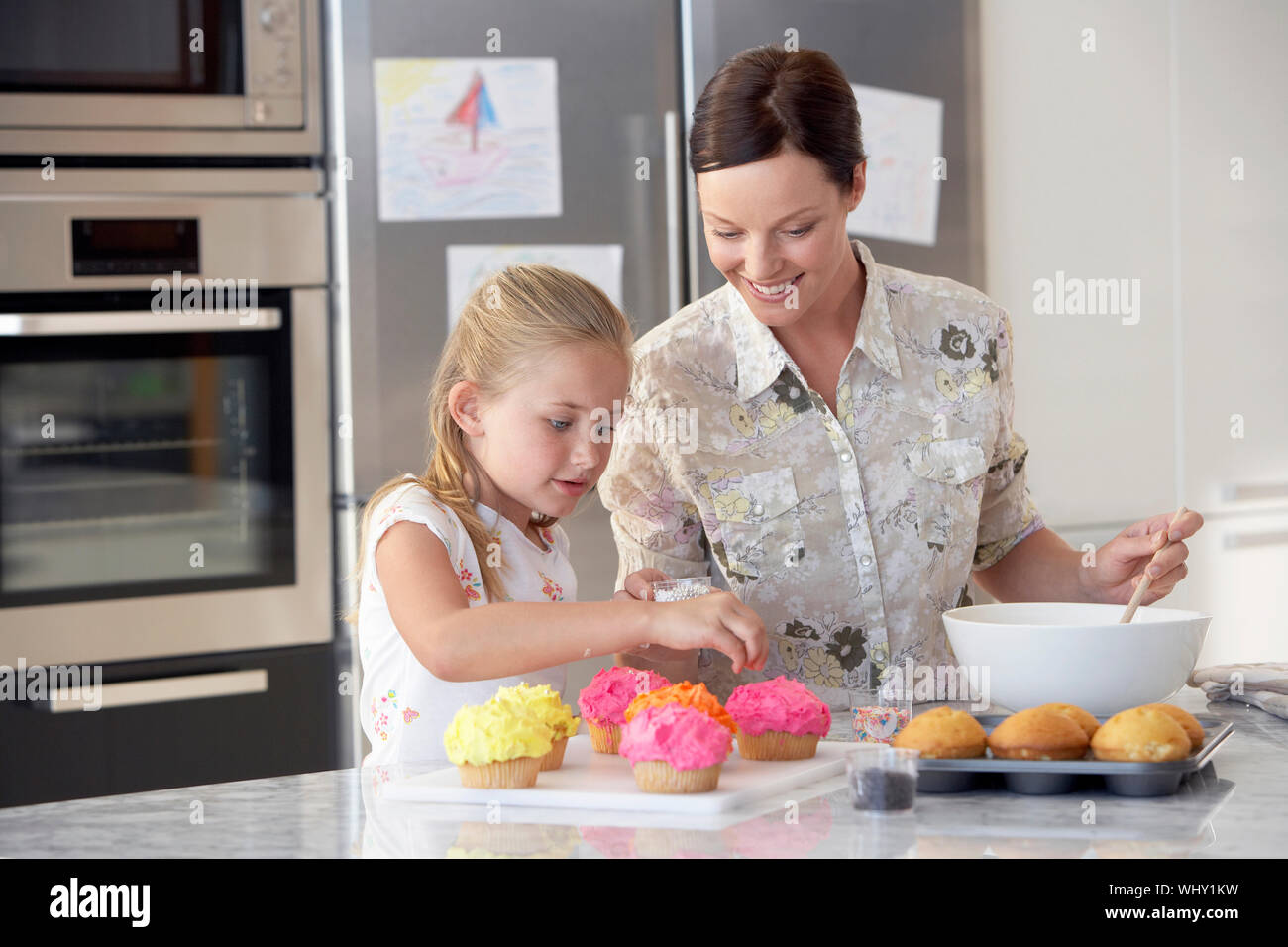 Happy mother and daughter preparing cupcakes in kitchen Stock Photo