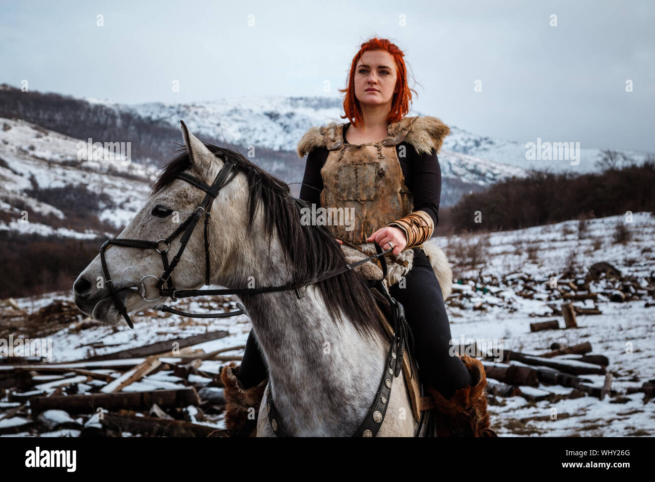 Beautiful girl on horse and with red hair in armor. Woman is a Viking. Fantasy Stock Photo