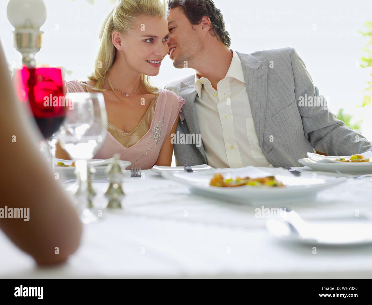 Young man whispering into woman's ear at dinner party Stock Photo
