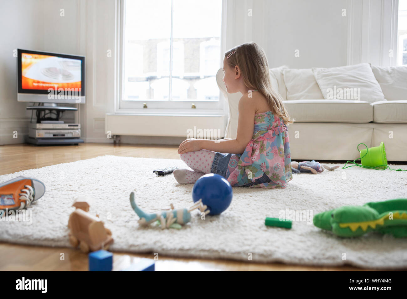 Side view of a little girl watching television with toys on floor Stock ...