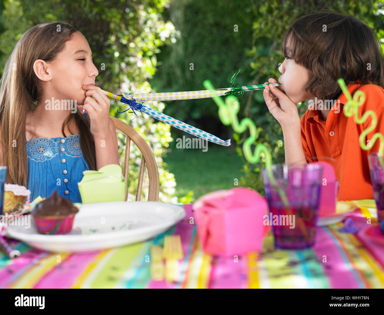 Young boy and girl blowing party puffers at each other in outdoor birthday party Stock Photo