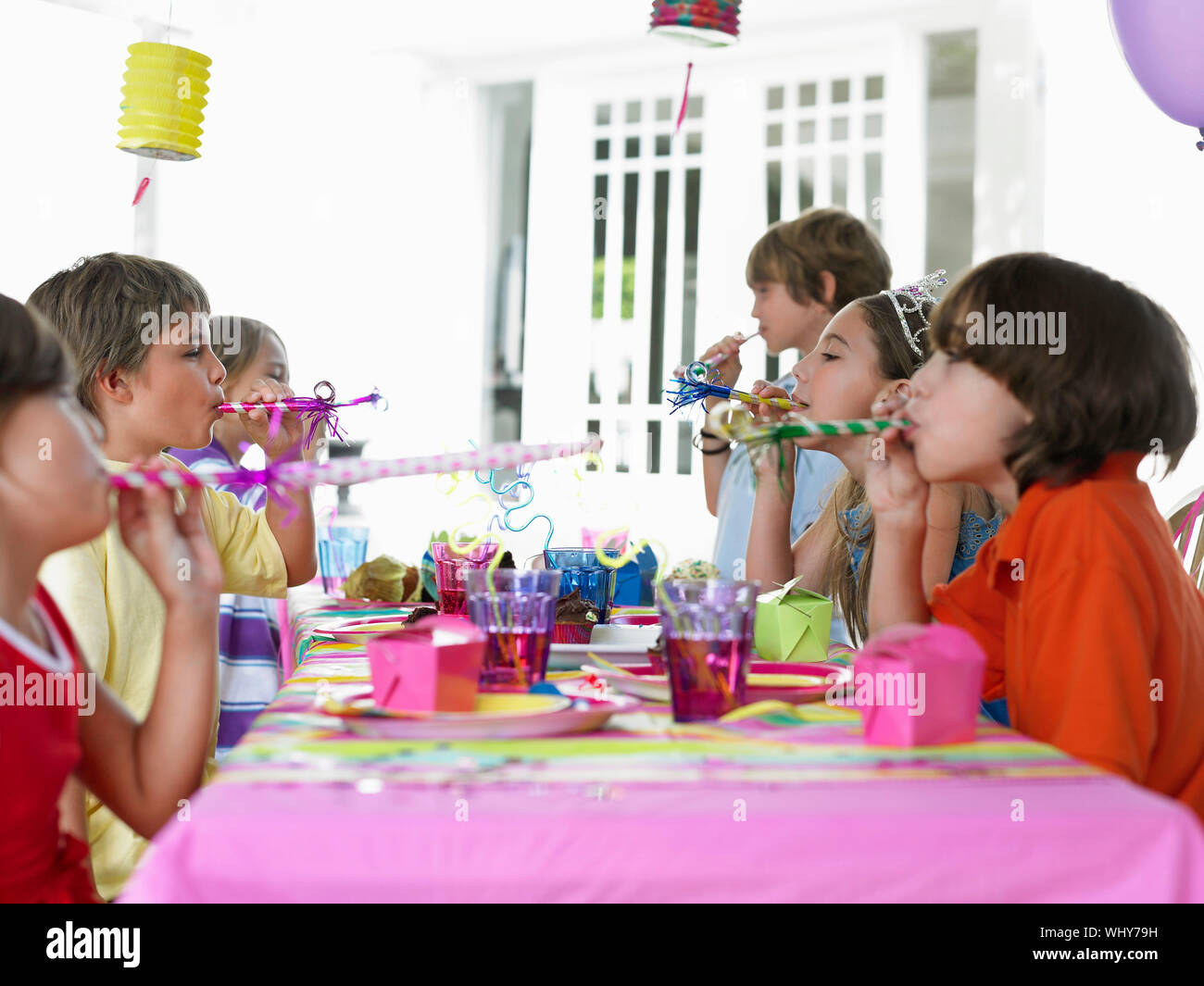 Side view of six children at outdoor table blowing party puffers Stock Photo