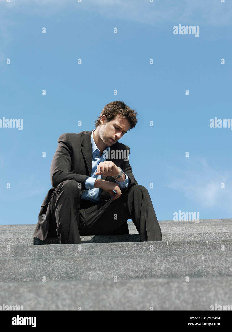 Young businessman sitting on steps looking at wristwatch Stock Photo ...