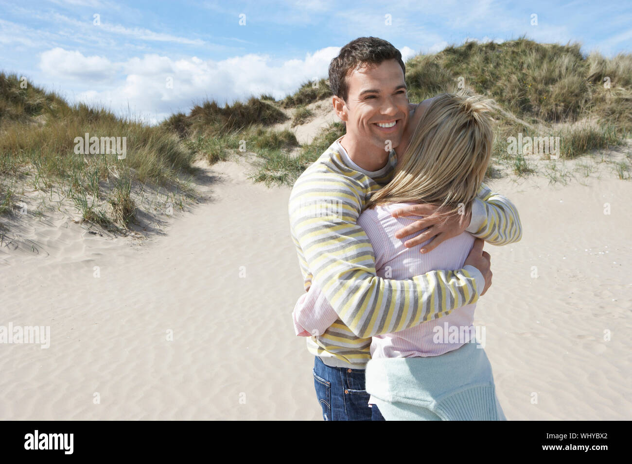 Smiling young man hugging woman on sandy beach Stock Photo - Alamy