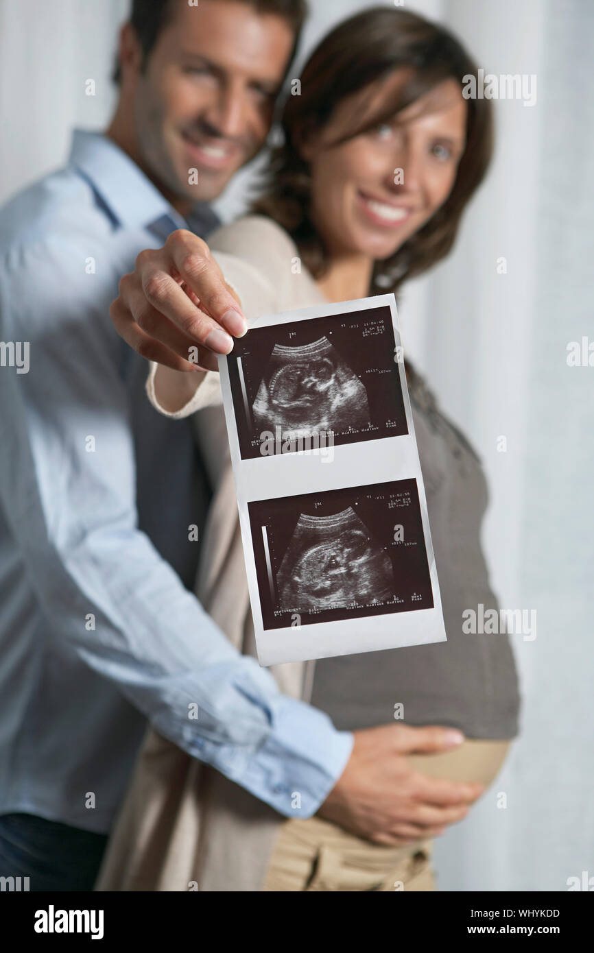 Man embracing woman as she holds up ultrasound scan photo of baby Stock ...