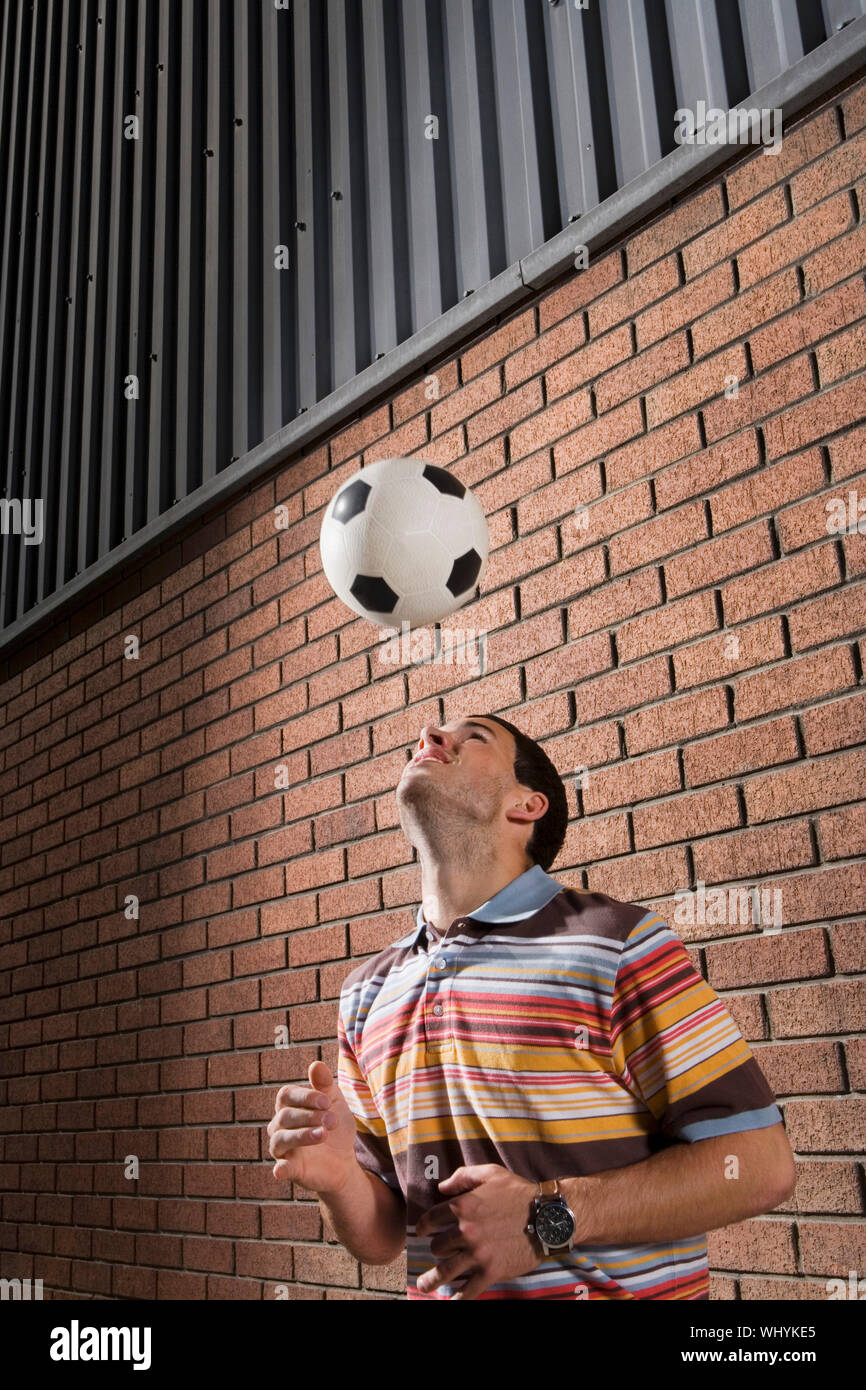 Young man bouncing ball off head against brick wall Stock Photo Alamy