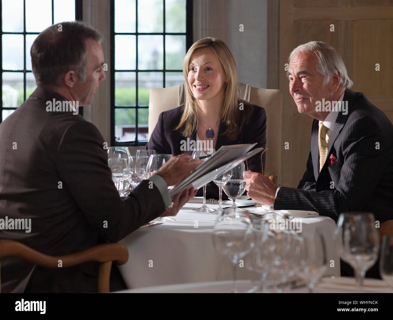 Three businesspeople sitting at restaurant table and discussing documents Stock Photo