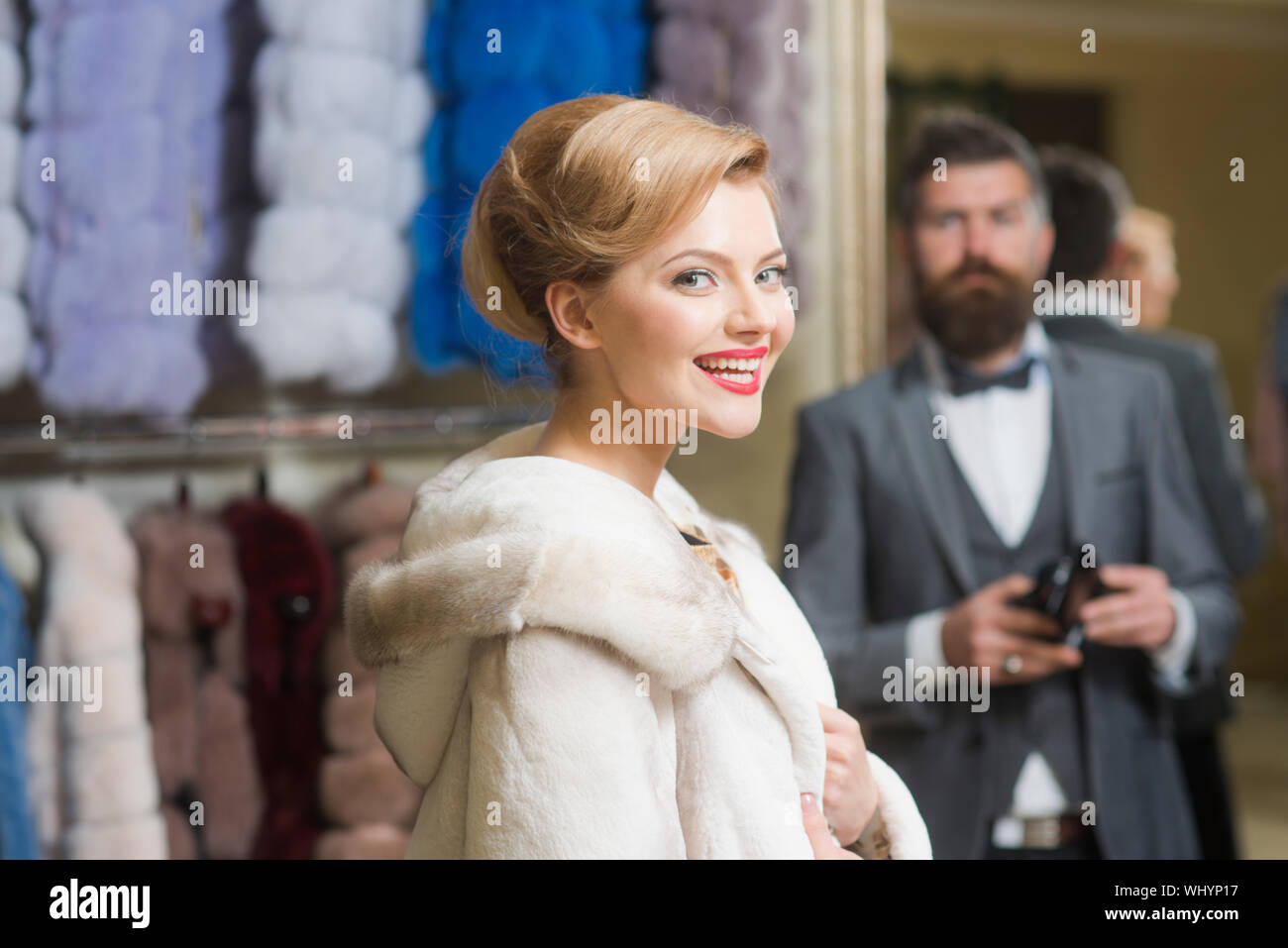 Couple in love tries expensive pink mink overcoat on. Man with wallet and girl with happy faces on clothes rack background. Customer with beard and wo Stock Photo