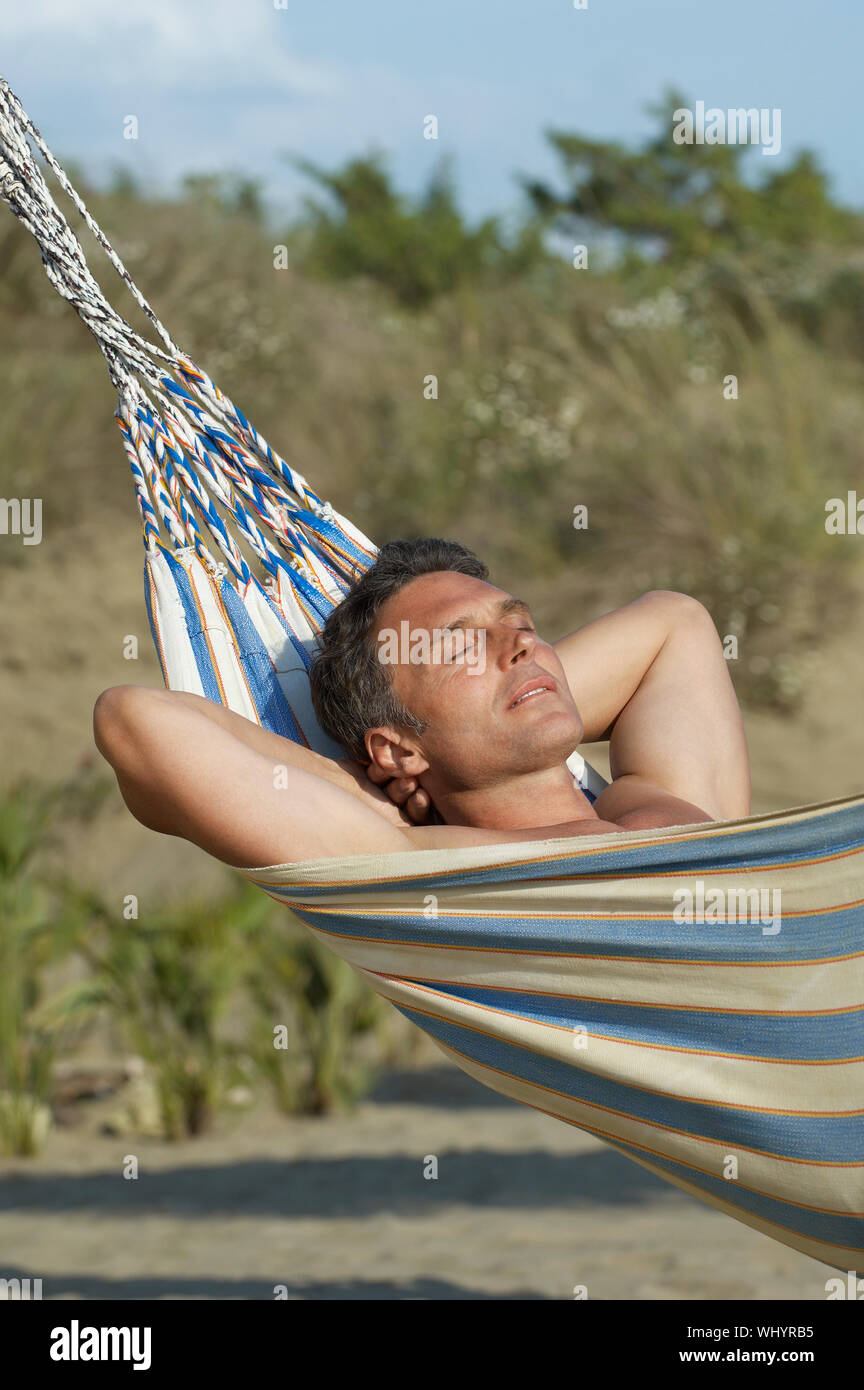 View of a man relaxing in hammock against blurred plants Stock Photo