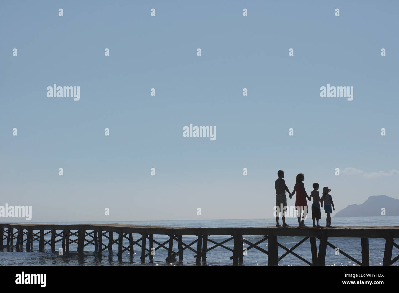Full length of silhouetted parents and two children holding hands on jetty Stock Photo