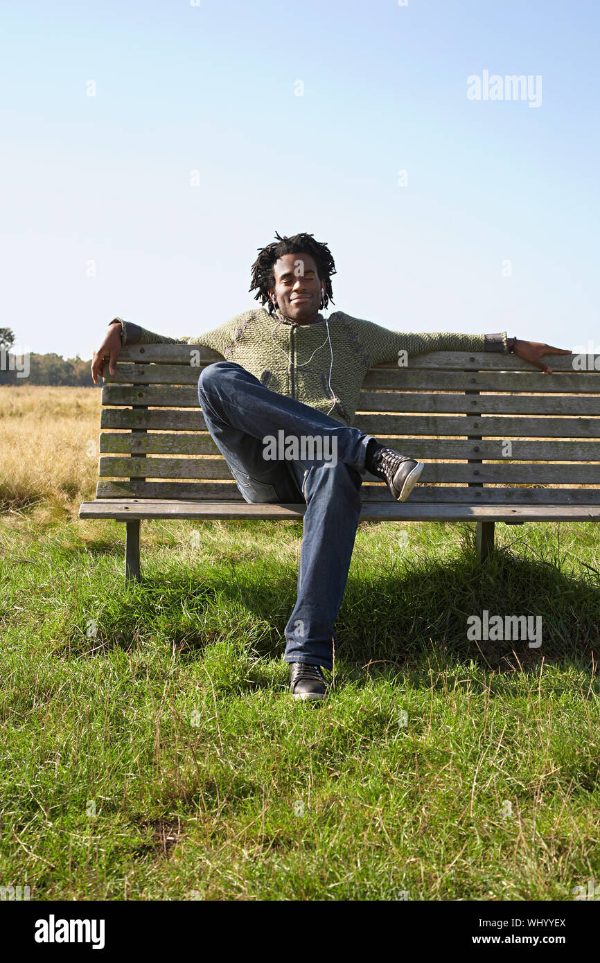 Full length of young man listening to music while sitting on park bench ...