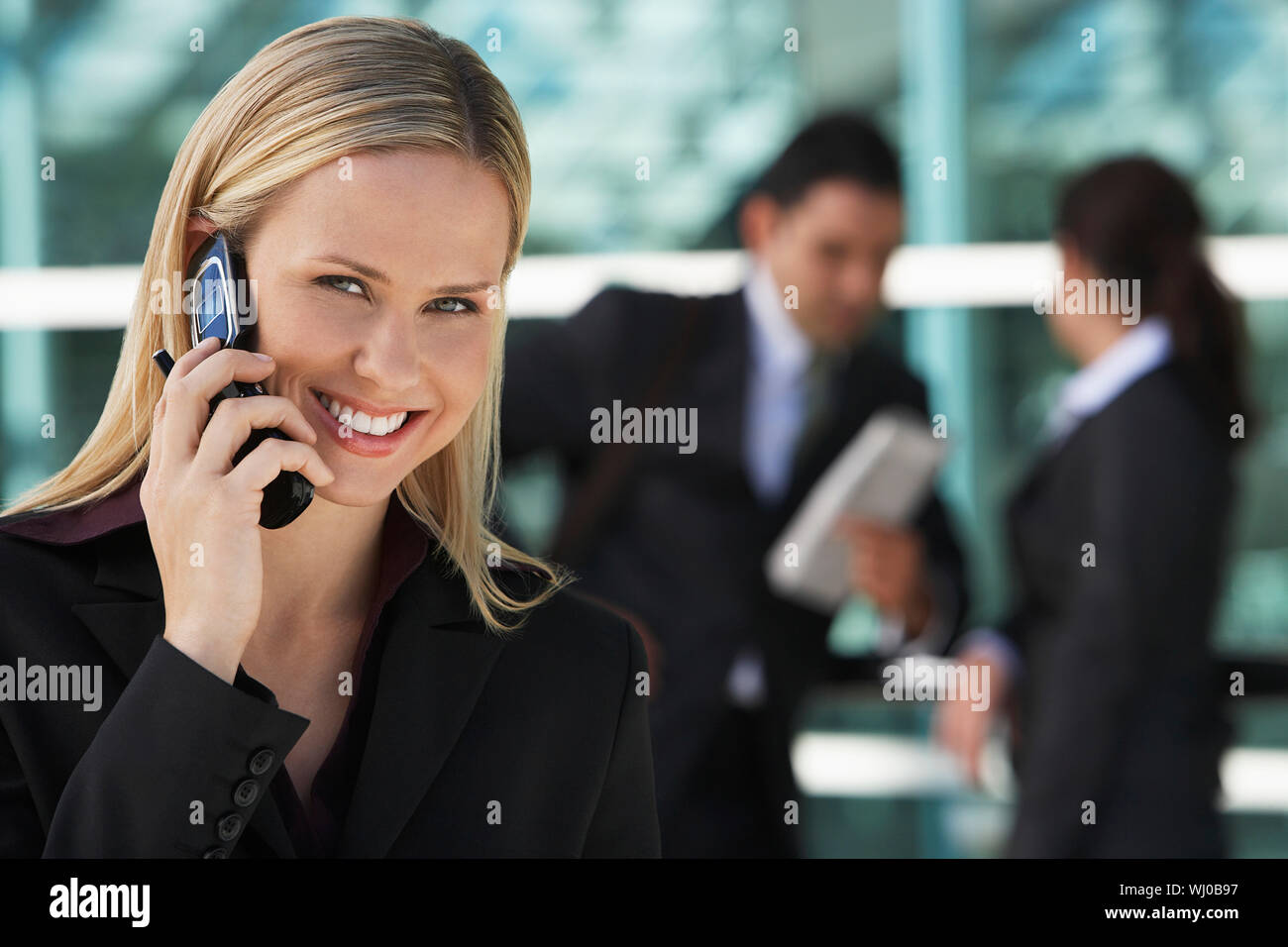 Businesswoman using mobile phone with colleagues in background, outdoors Stock Photo