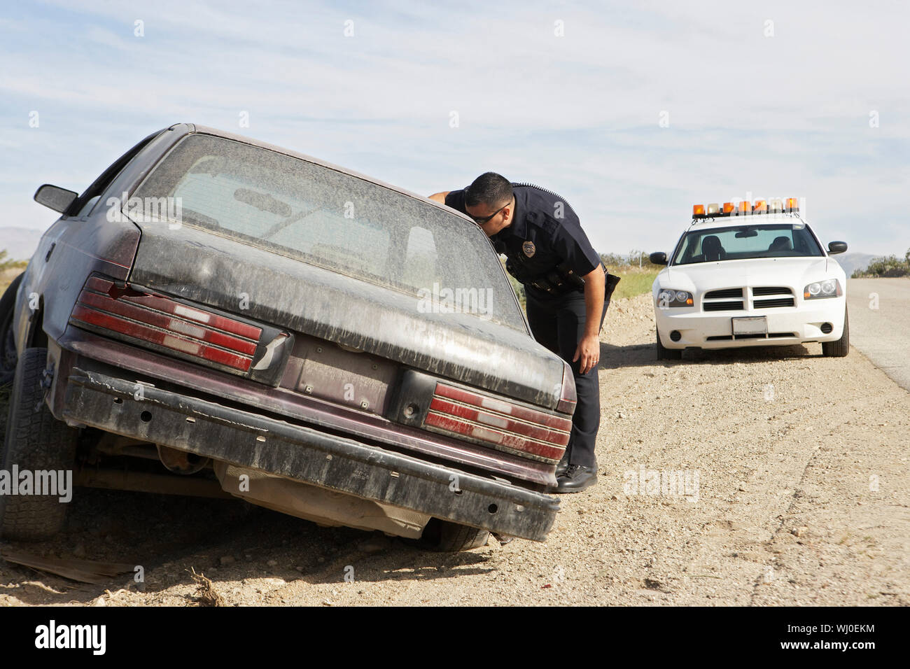 Police officer looking into abandoned car on roadside Stock Photo - Alamy