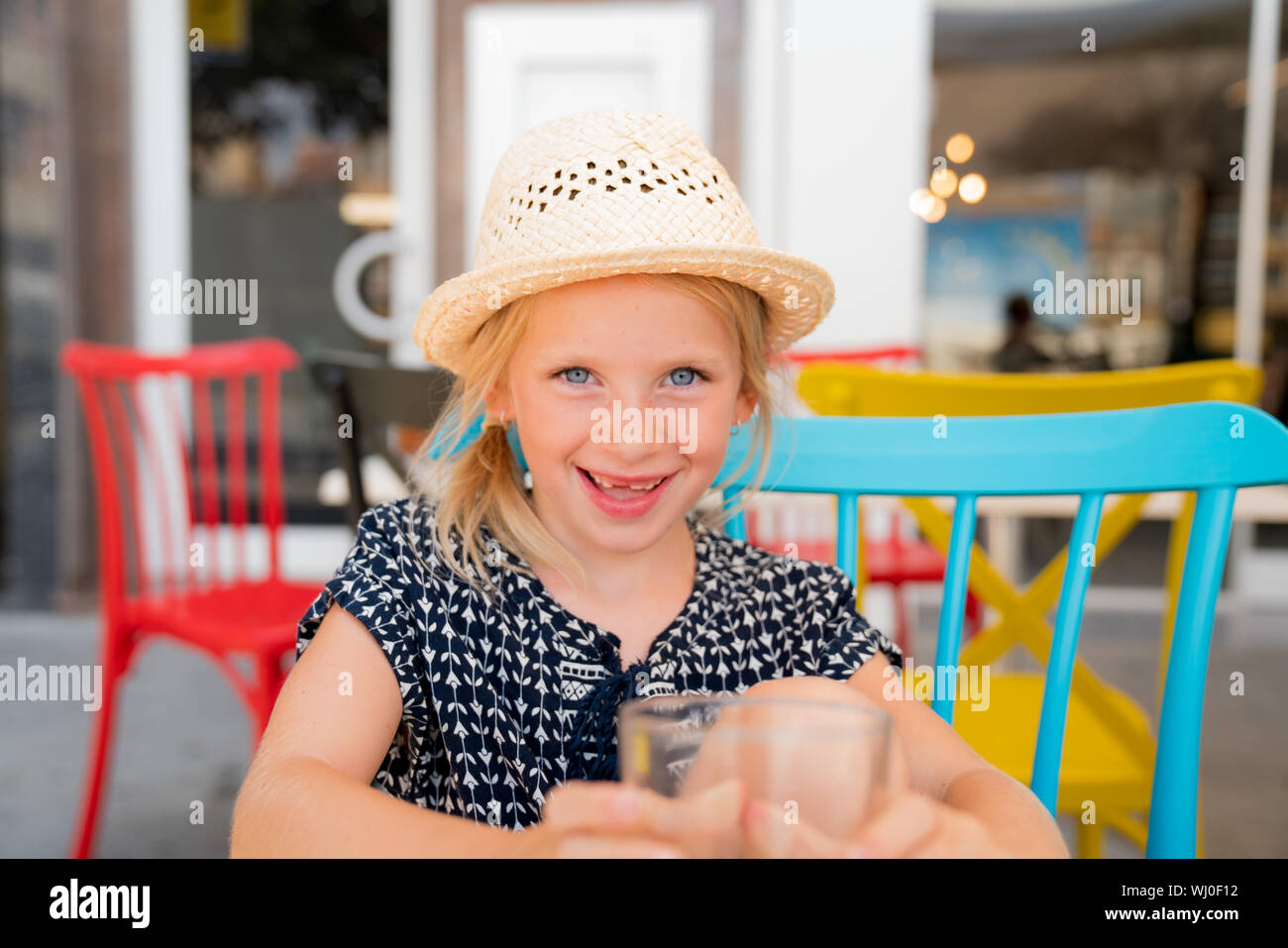 Portrait of a child that is having a good time on a cafe terrace. girl is wearing a hat for the sun, having fun with the family on a cafe terrace. Stock Photo