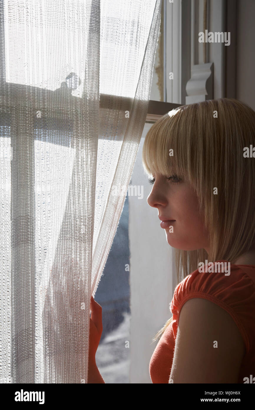 Beautiful teenage girl looking through window at home Stock Photo - Alamy