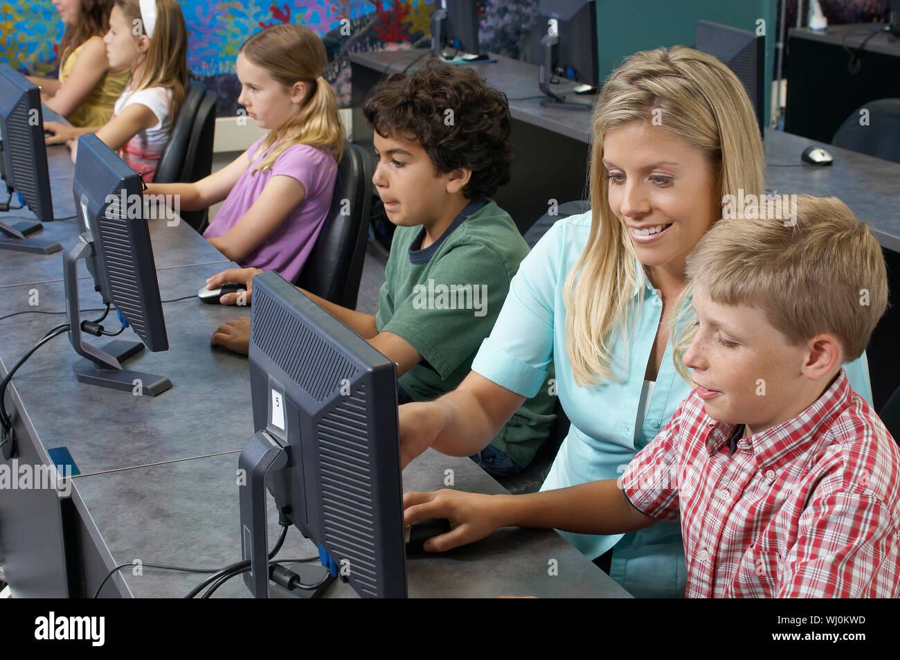 School children using computers with teacher in classroom Stock Photo ...