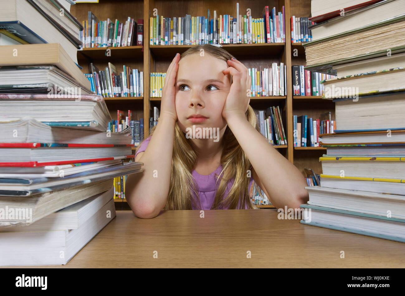 School girl sitting at desk with books in library Stock Photo - Alamy